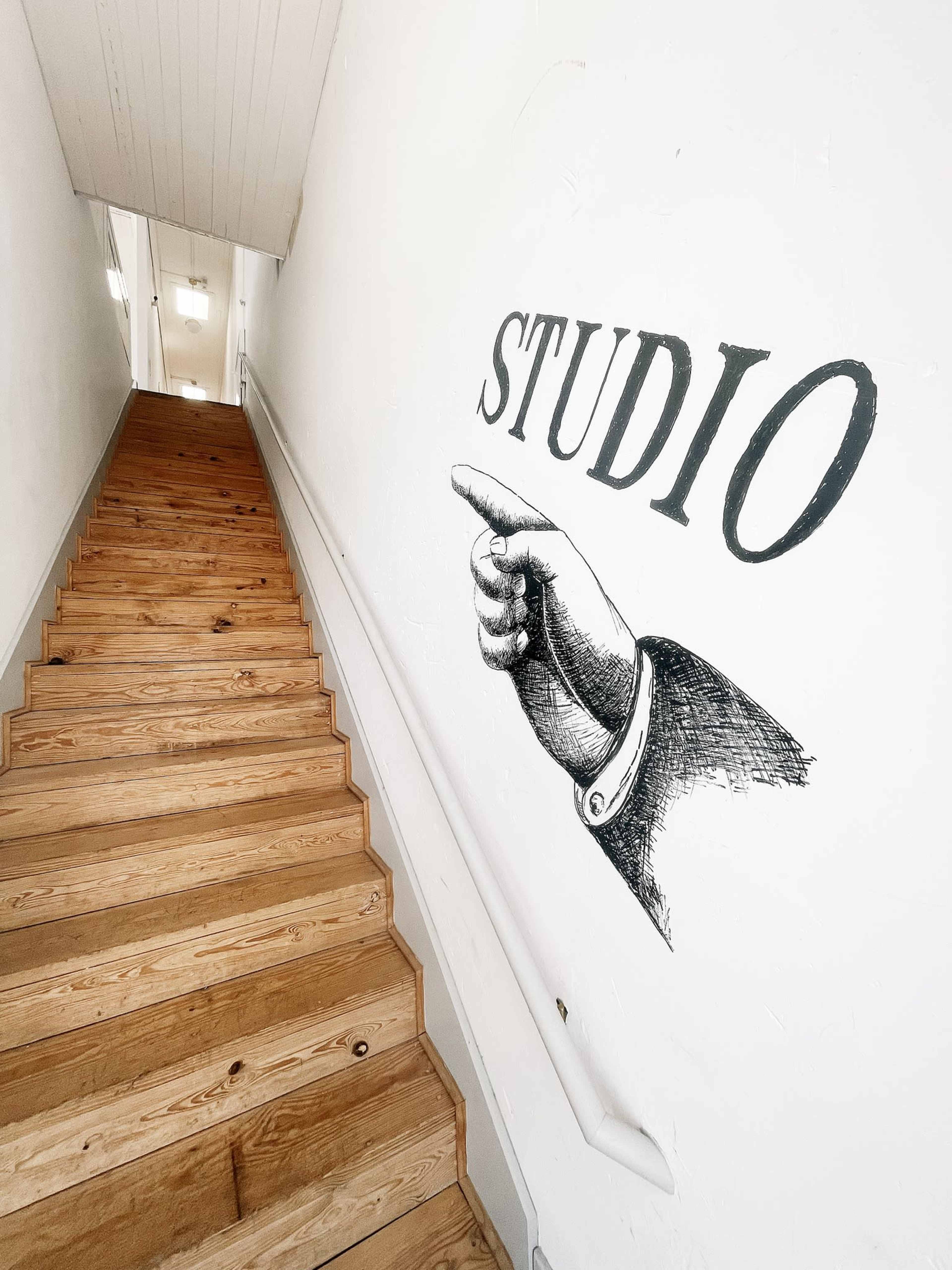 A staircase with wooden steps leads upward, alongside a wall featuring the word "STUDIO" and an illustration of a pointing hand.
