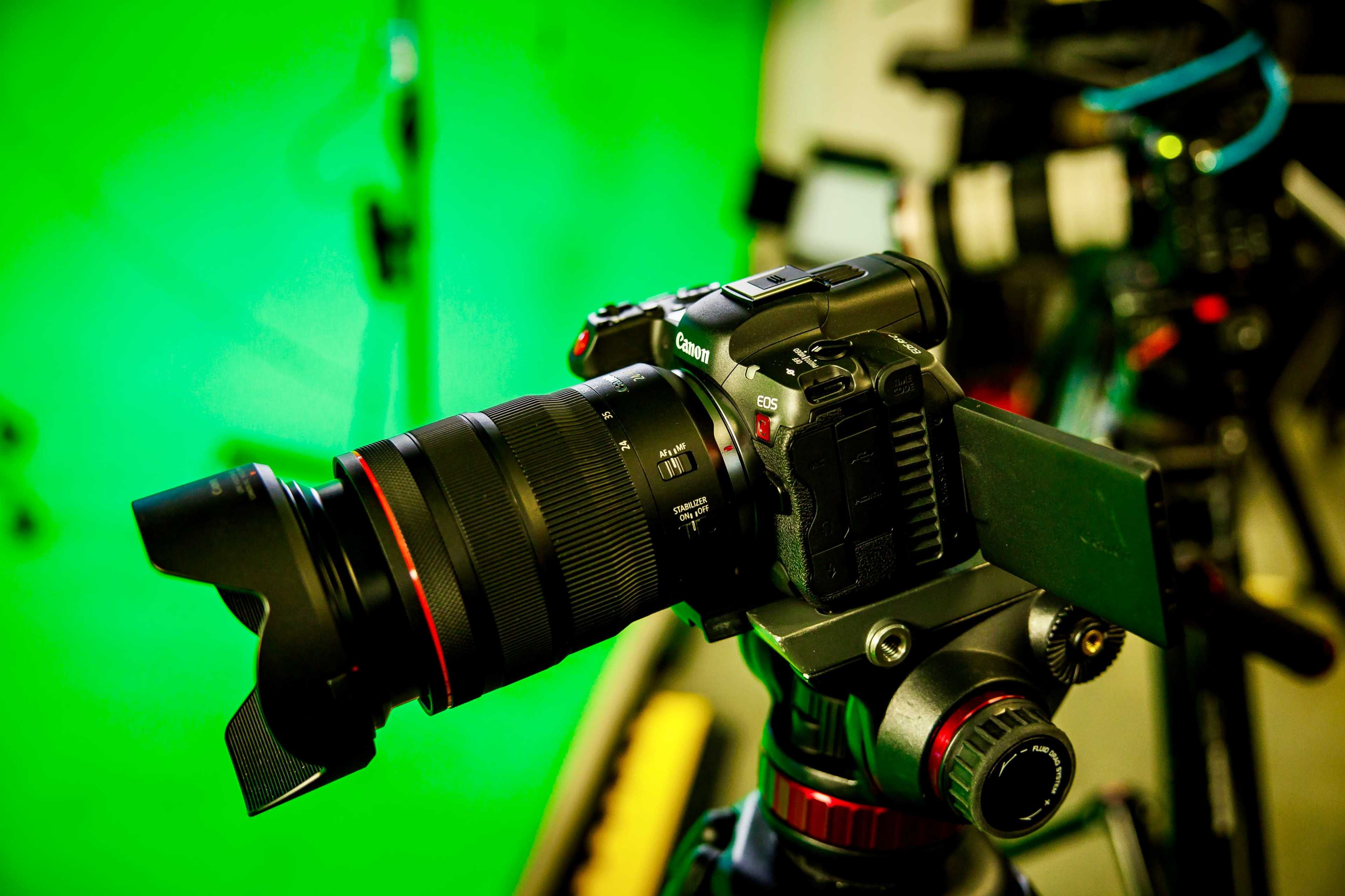 A Canon camera is mounted on a tripod in front of a green screen backdrop.