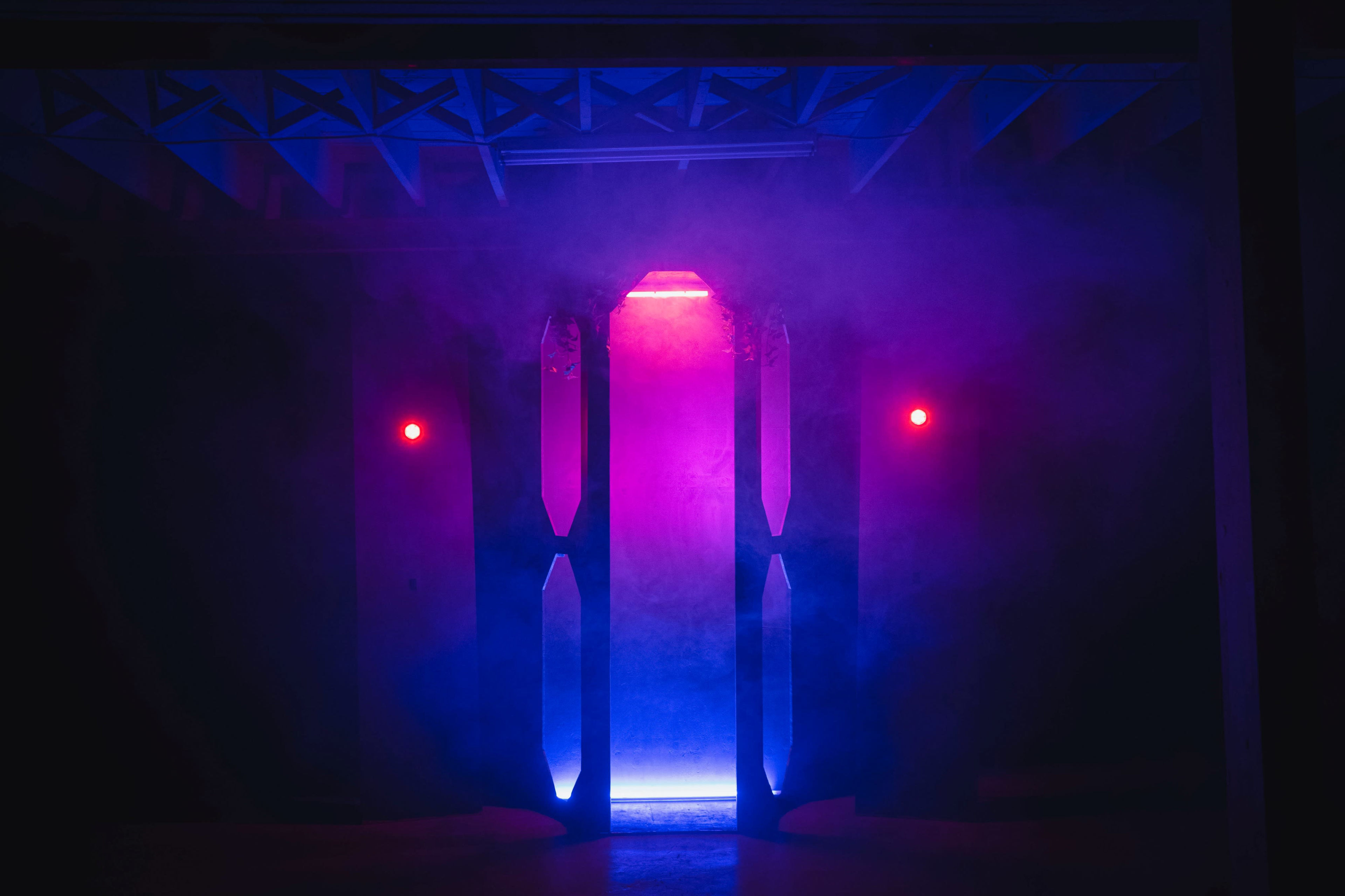 A doorway emits blue and pink light, surrounded by fog and illuminated by red wall lights.