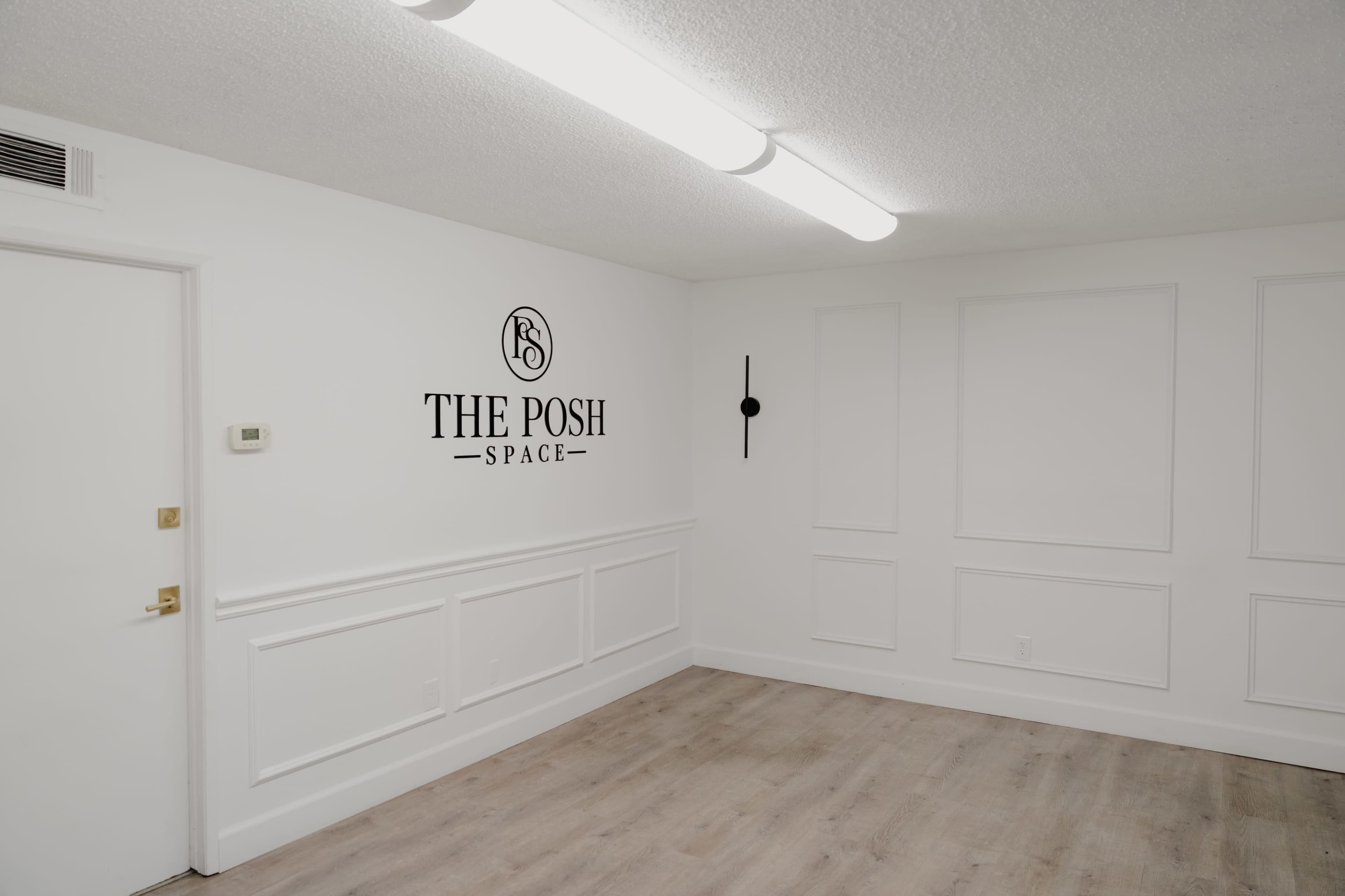 The image shows a minimalist interior room featuring white walls, a wooden floor, and a decorative wall element with the text "THE POSH SPACE" displayed prominently.