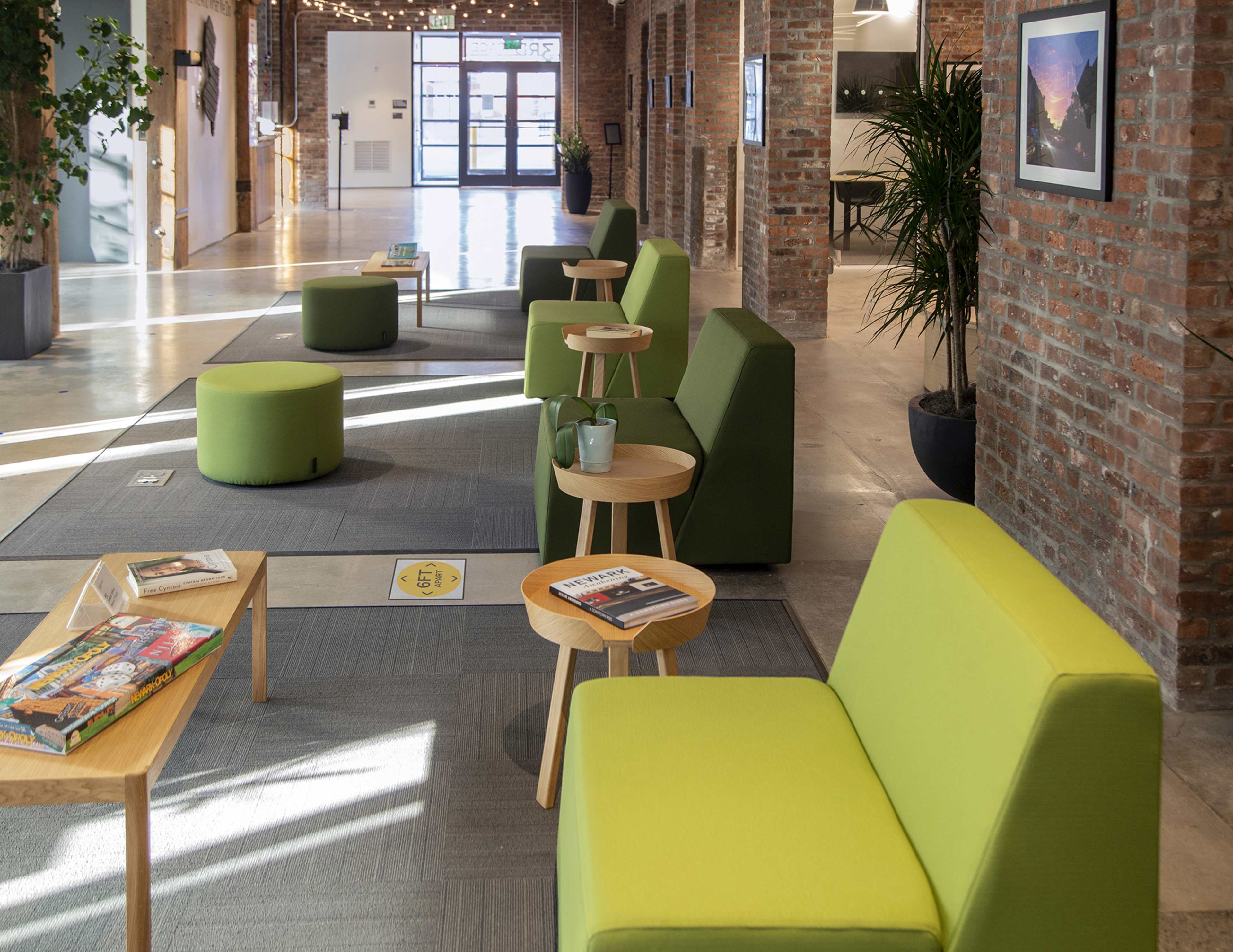 A modern interior space featuring green lounge seating and wooden side tables arranged along a brick wall.