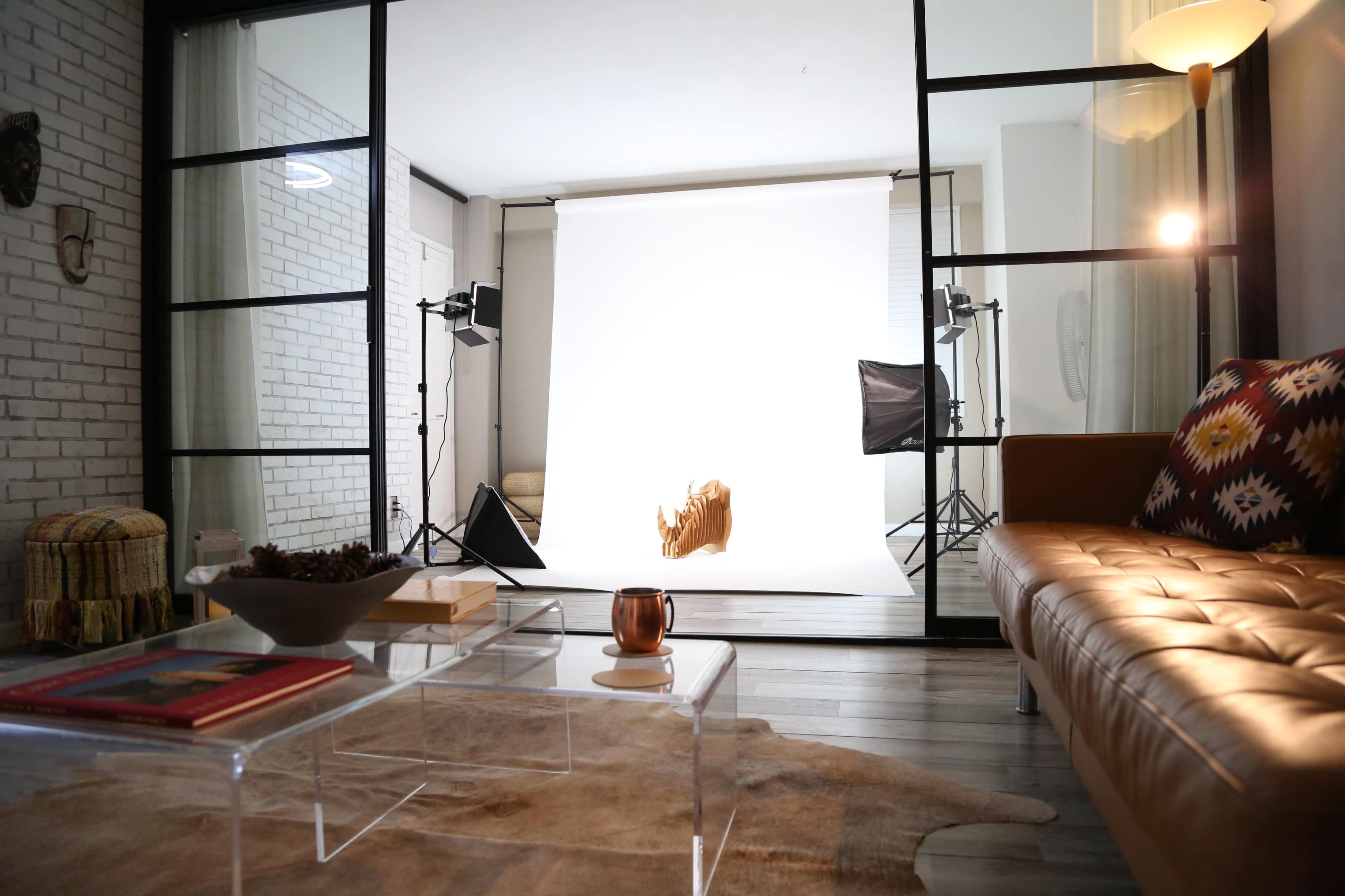 The image features a photography studio setup with a white backdrop, softbox lights, and a cozy living area visible in the foreground.
