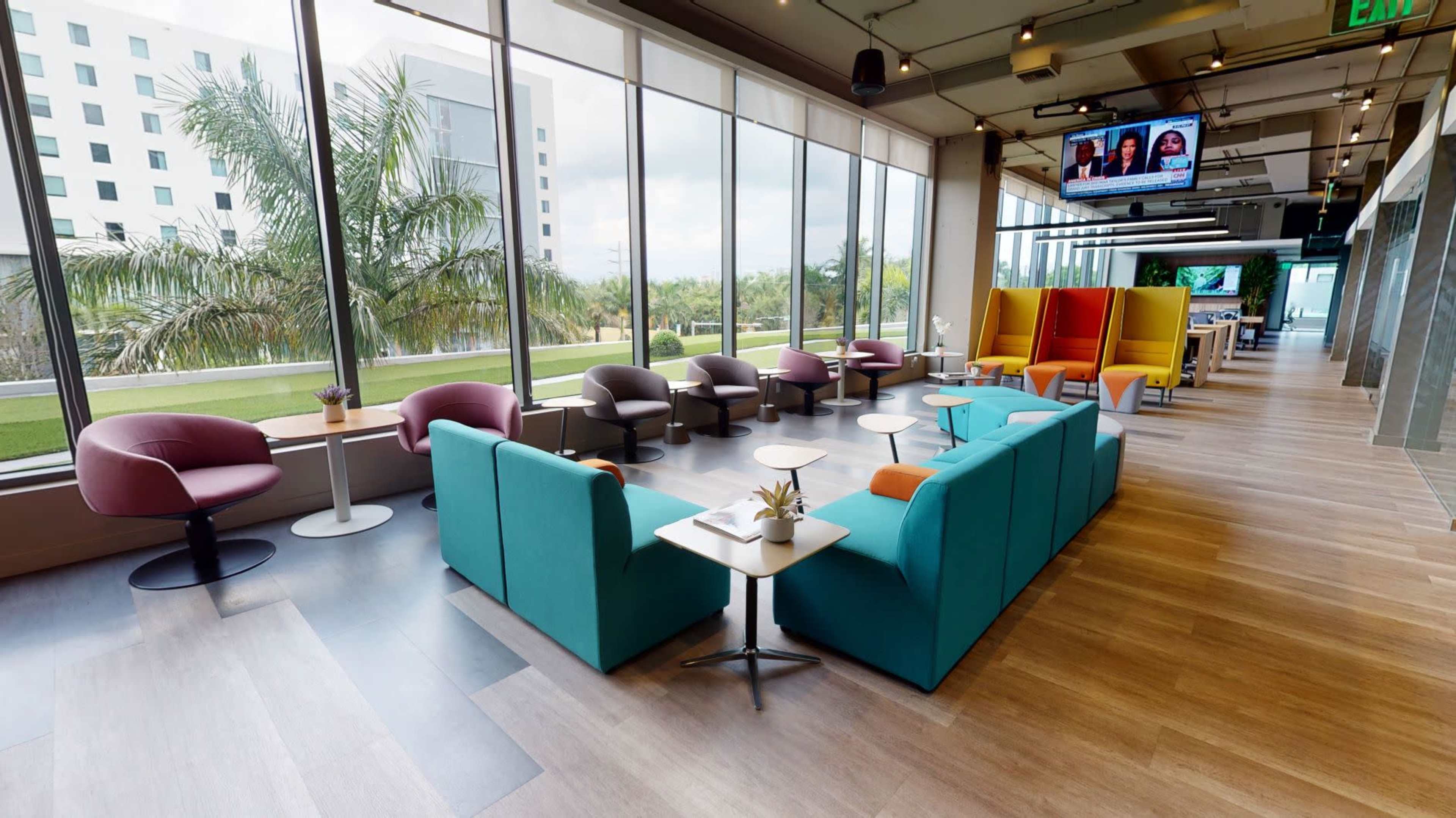 A modern lounge area with colorful seating, large windows, and a view of greenery outside.