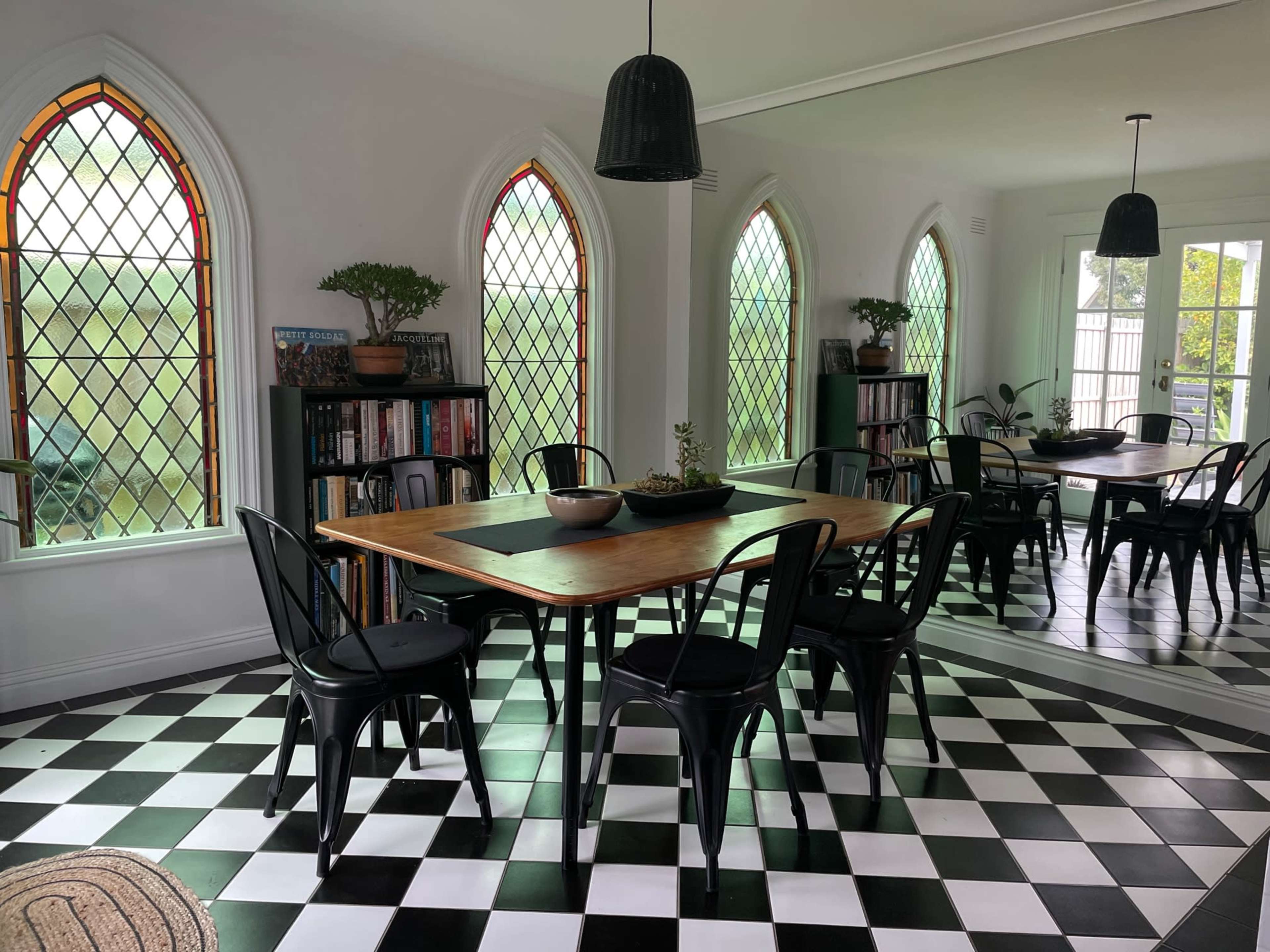 A dining area features a wooden table surrounded by black chairs, with stained glass windows and a checkered floor.