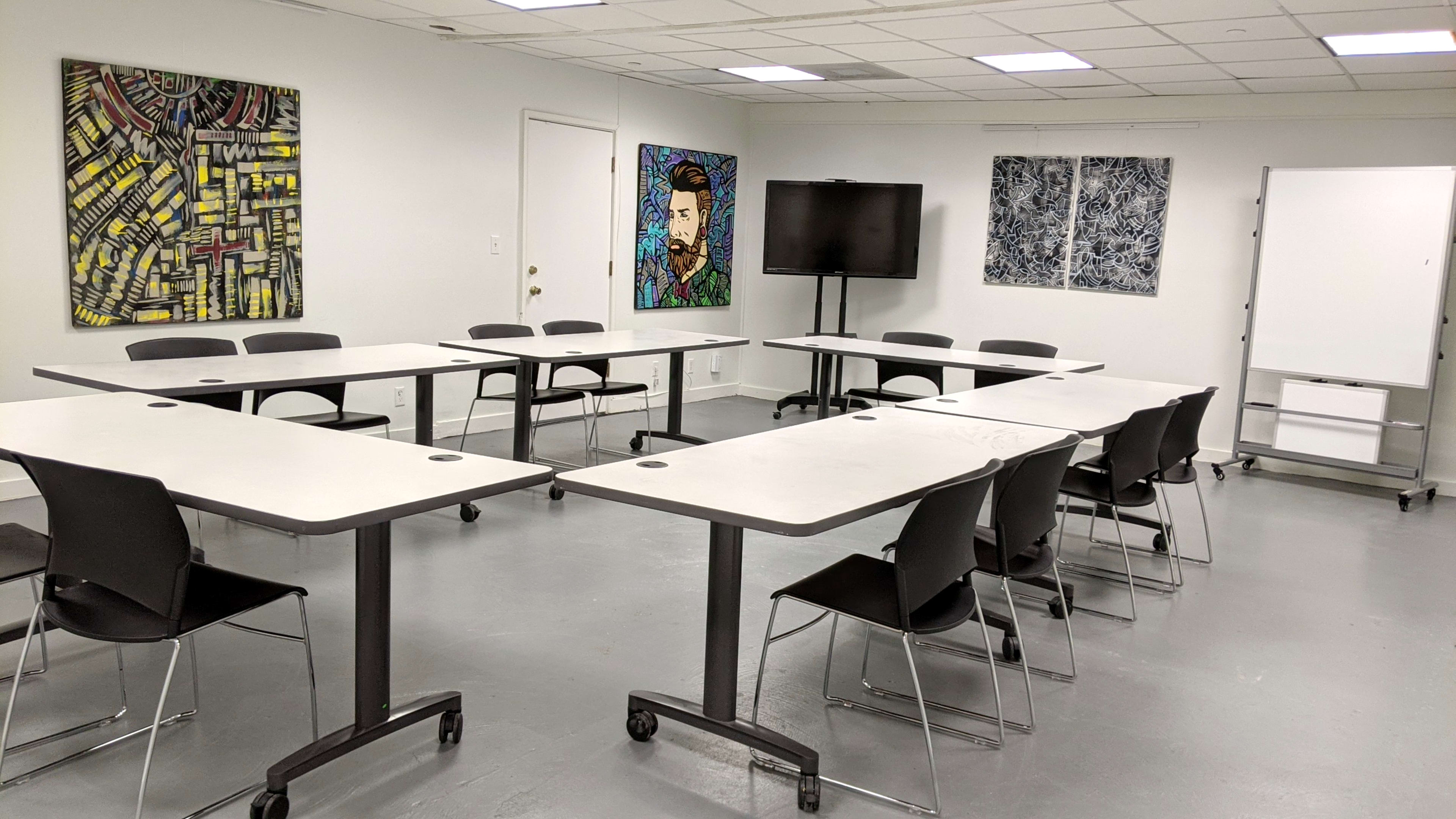 A modern conference room features several tables arranged in a U-shape, with black chairs and colorful artwork on the walls.