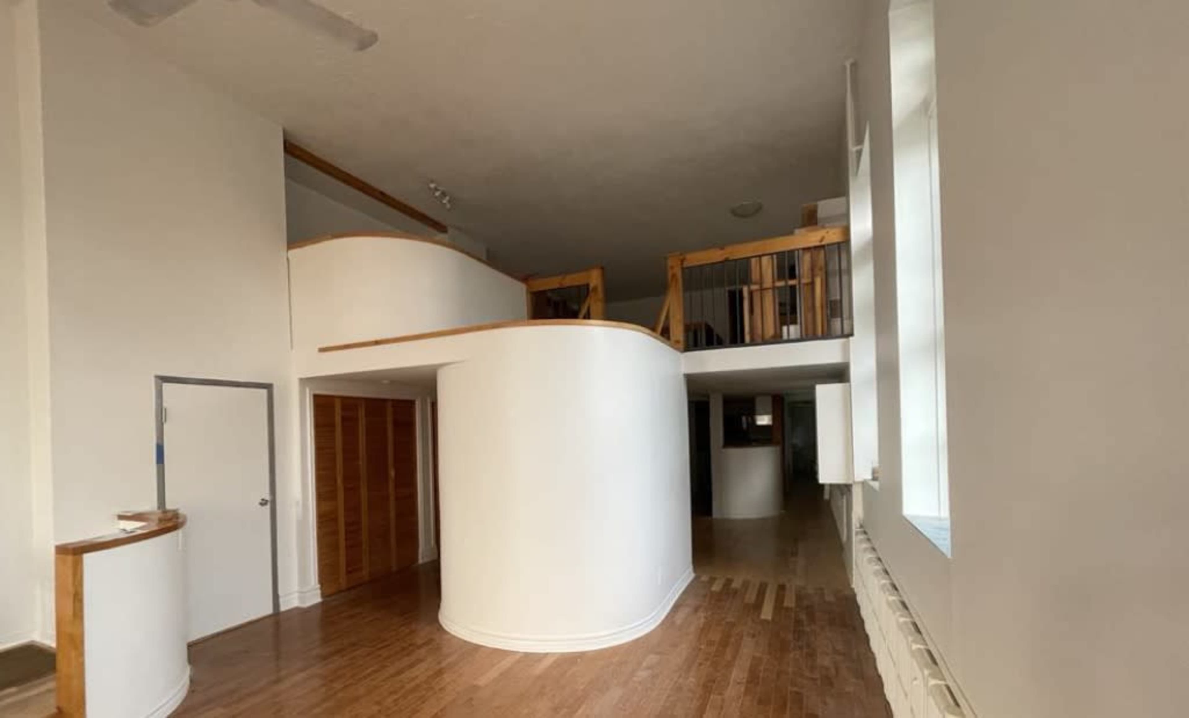 The image shows an interior space of a modern house with curved walls, wooden flooring, and multiple levels connected by a staircase.