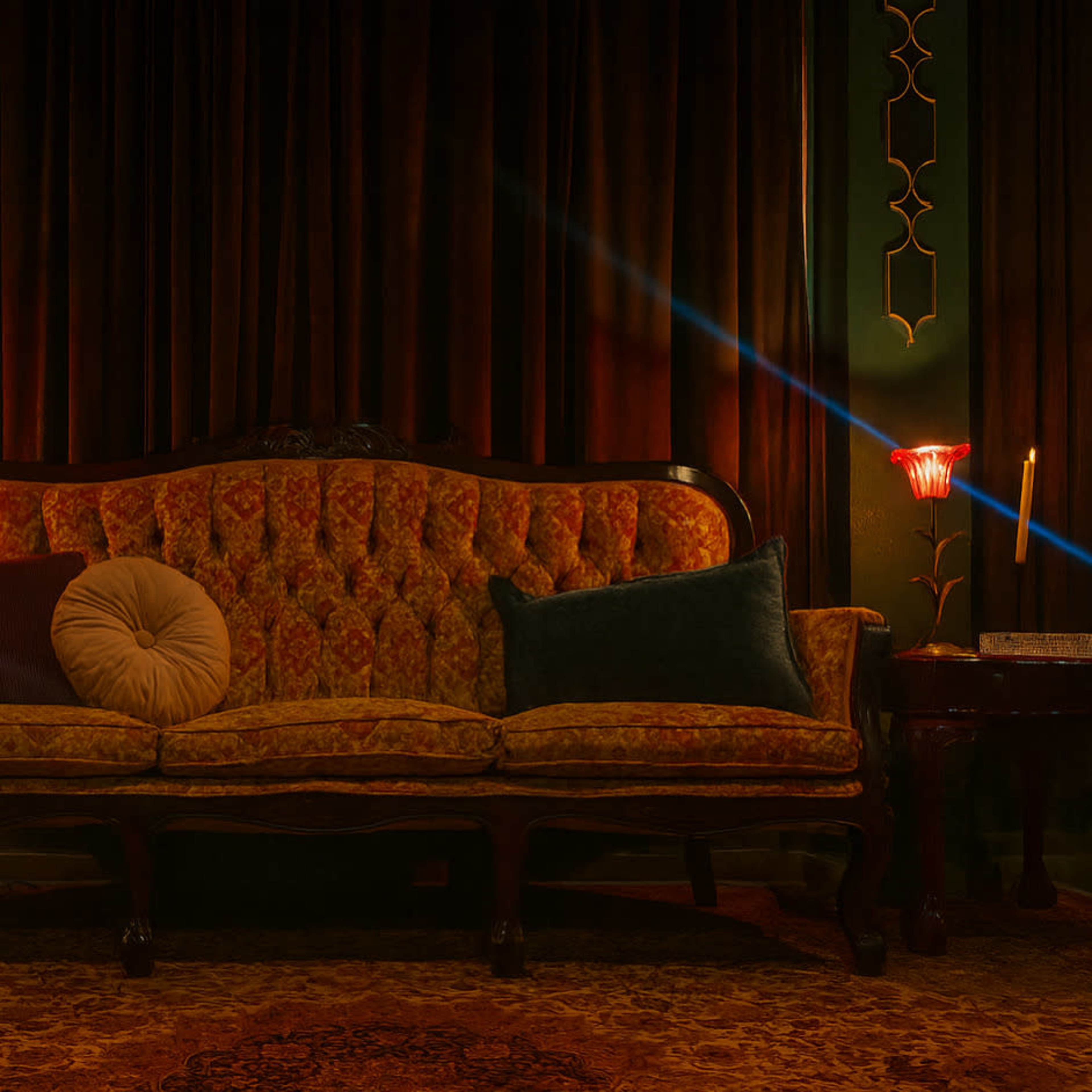A vintage sofa with ornate upholstery sits in a dimly lit room next to a small table featuring a decorative lamp and a candle.