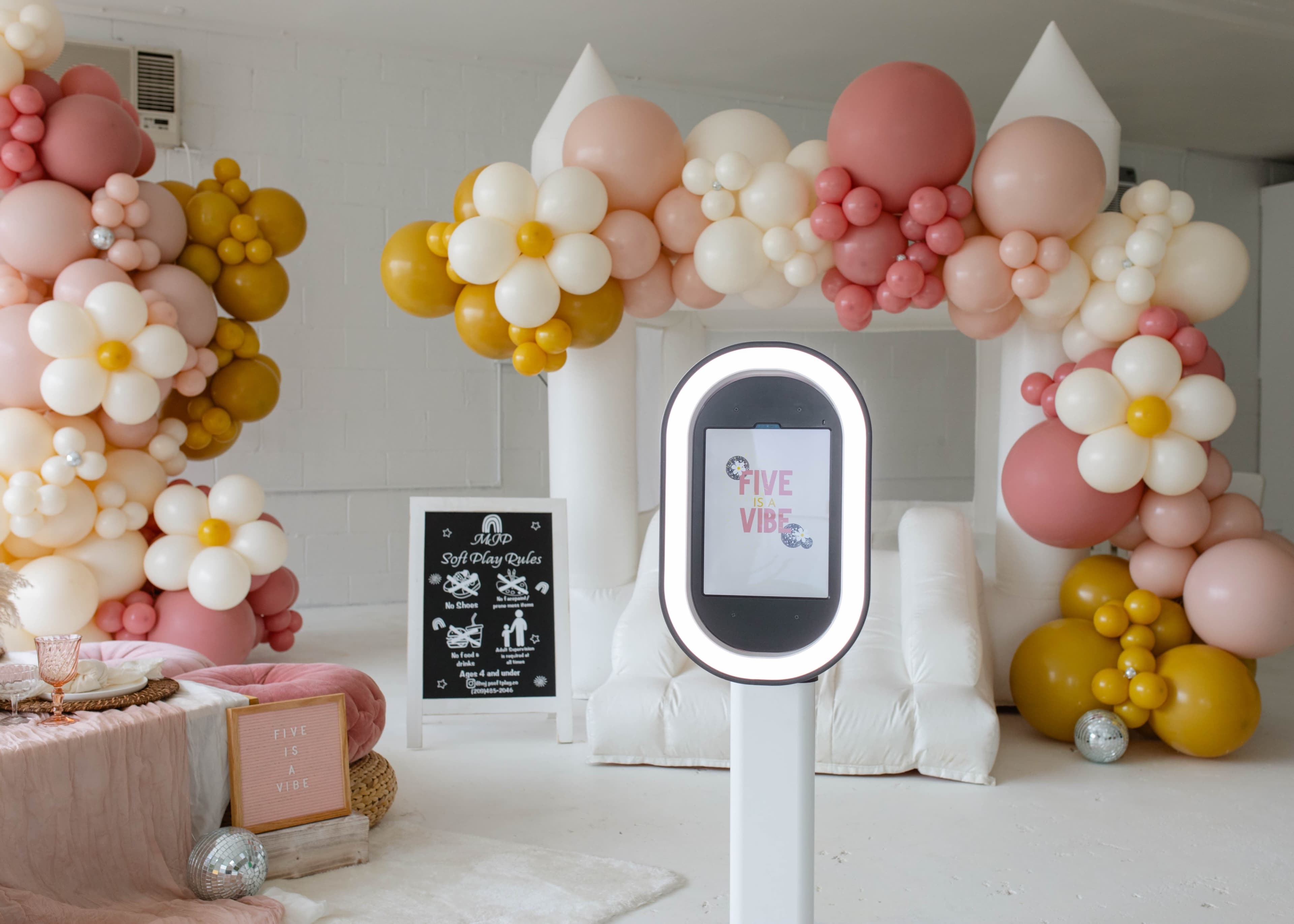 A festive party scene with a balloon arch and a digital signage display highlighting a "Five Vibe" theme in a decorated indoor space.