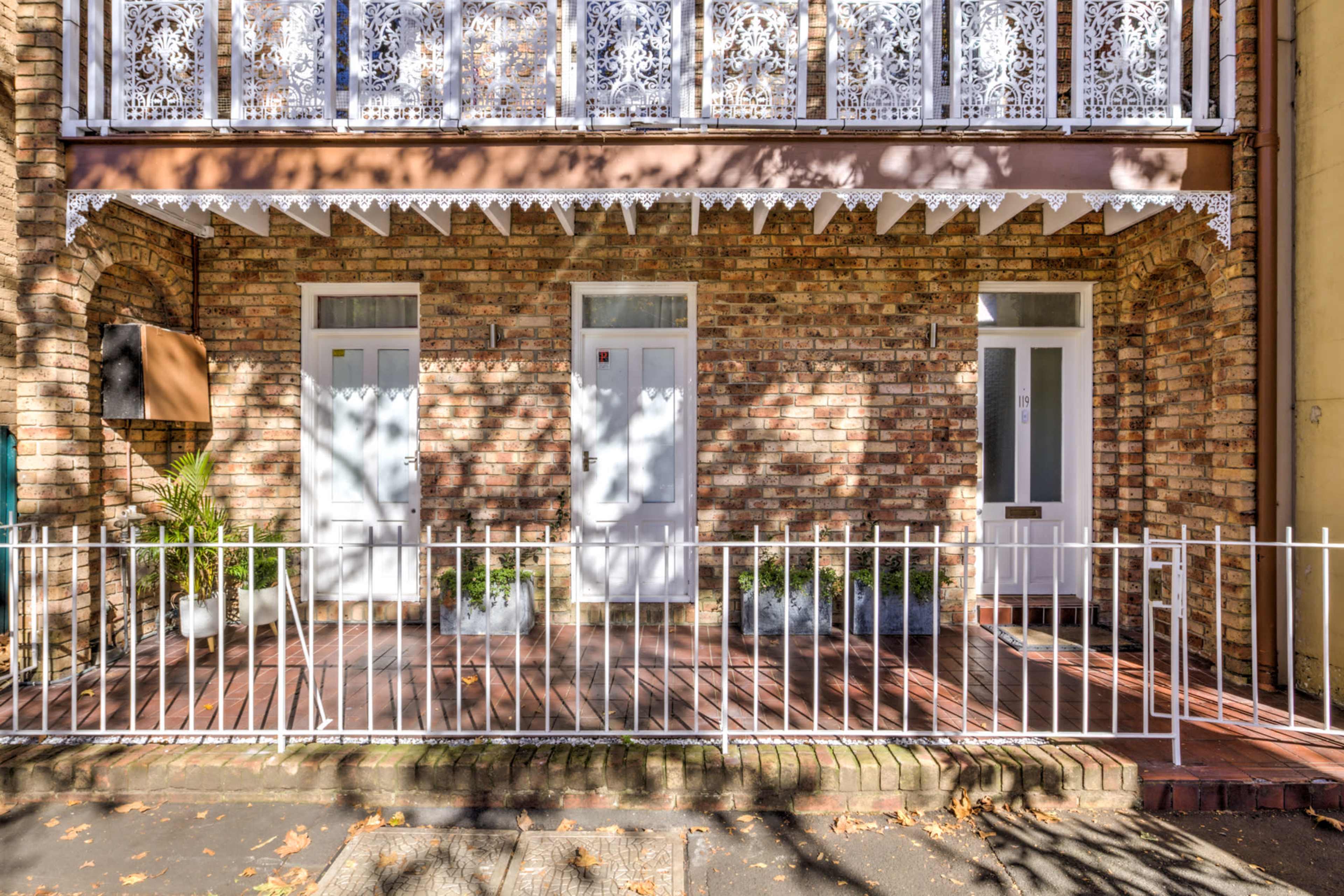 A brick facade with two white doors framed by decorative wrought iron railings and balcony details, set against a wooden deck.