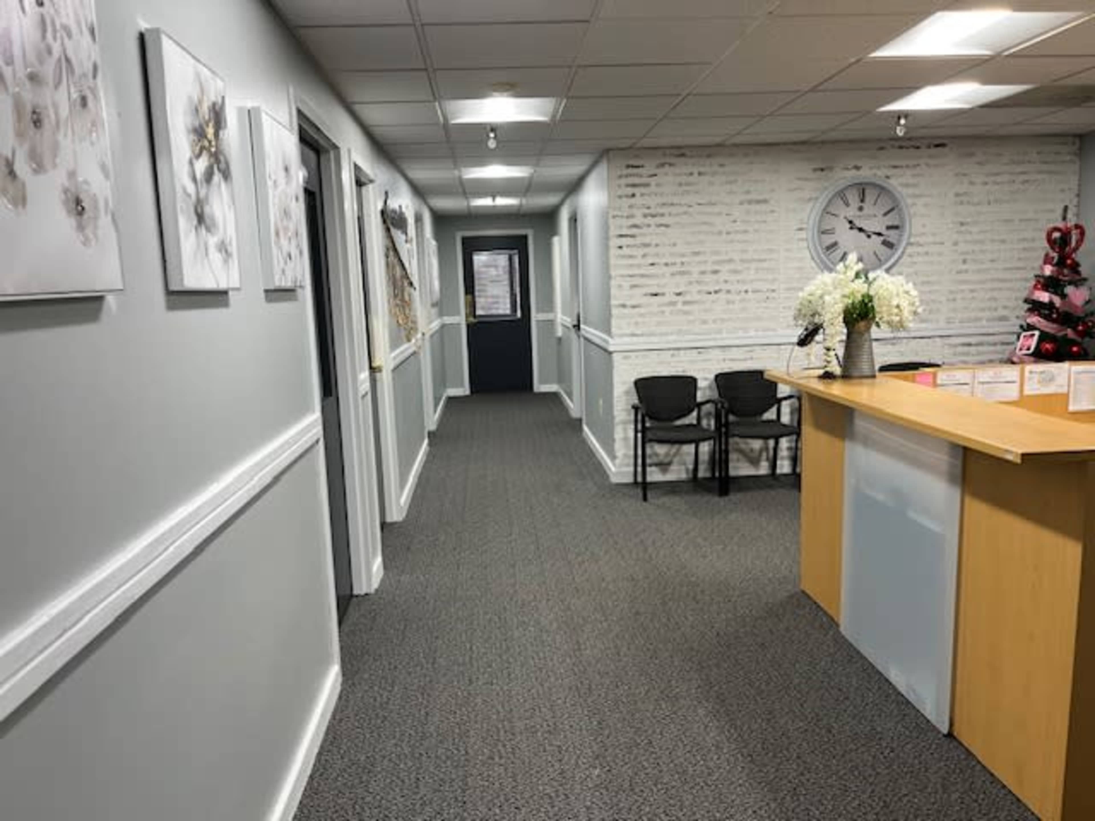 The image shows a well-lit hallway with decor on the walls, leading to a reception area featuring a counter and a Christmas tree in the corner.