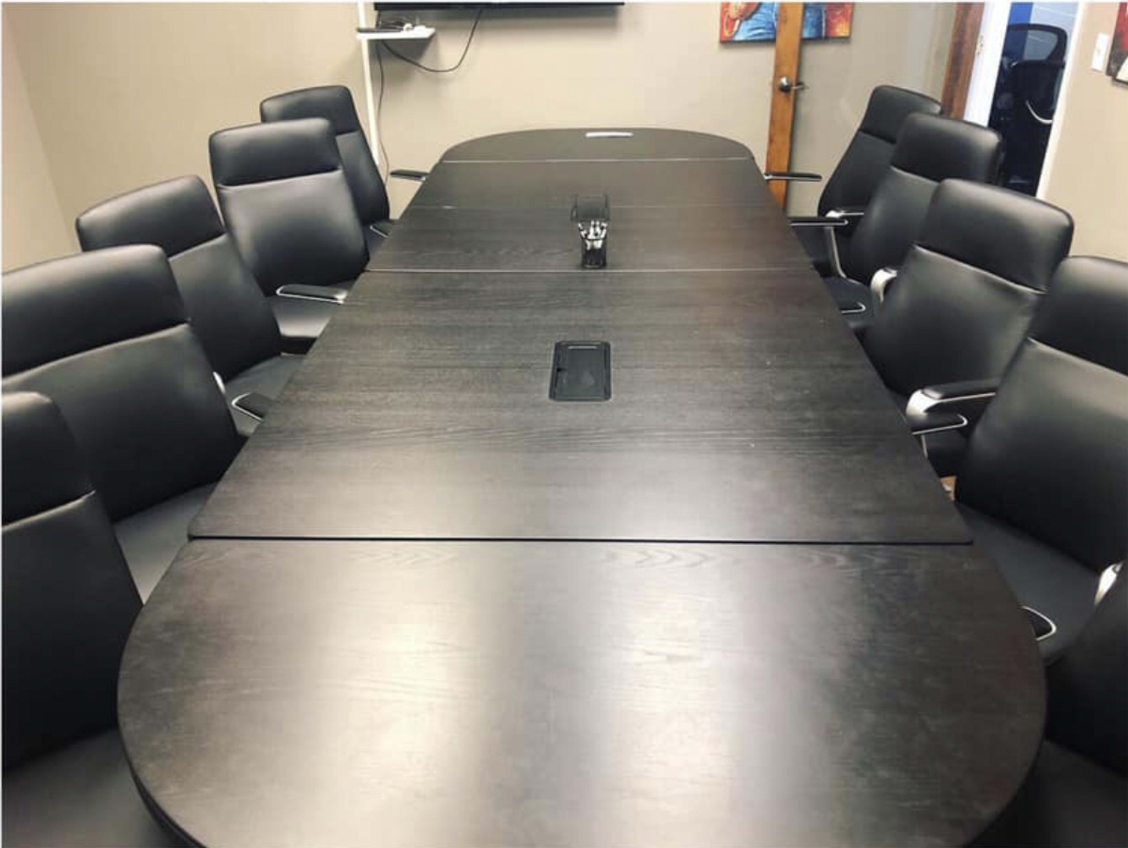 A large oval conference table surrounded by black ergonomic chairs is set up in a meeting room.