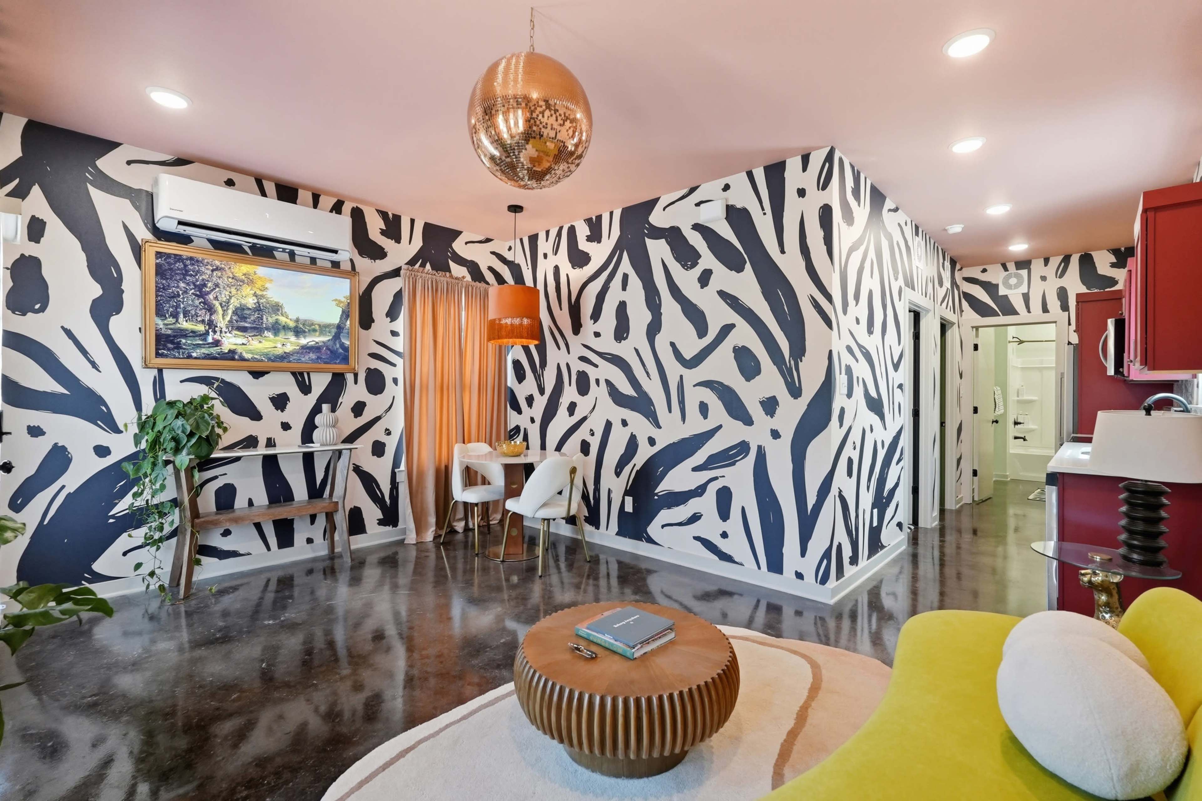 The image shows a stylish living space with bold patterned walls, modern furniture, and a decorative ceiling light.