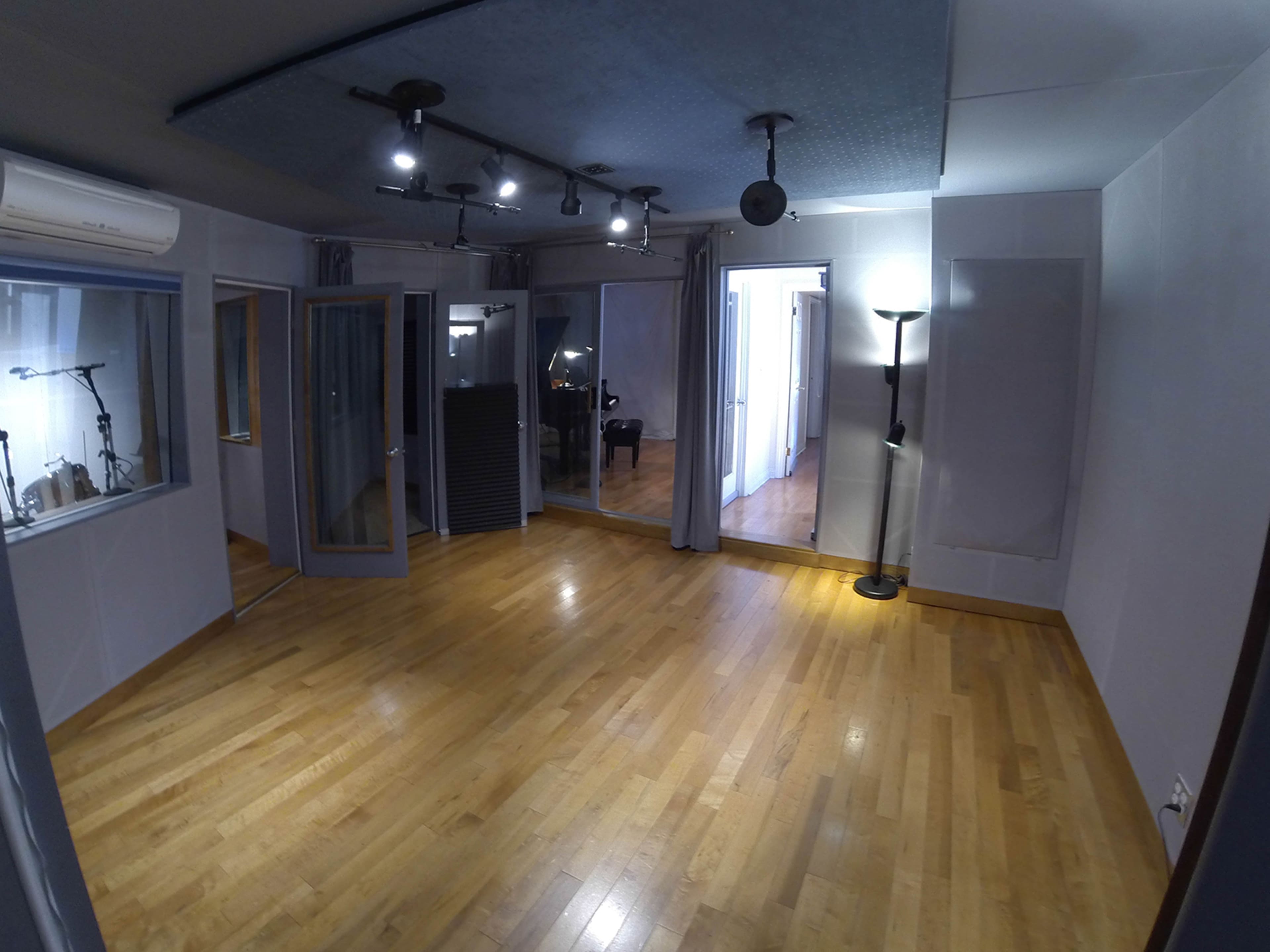 A sound studio with wooden flooring, multiple glass-paneled rooms, and professional lighting fixtures.