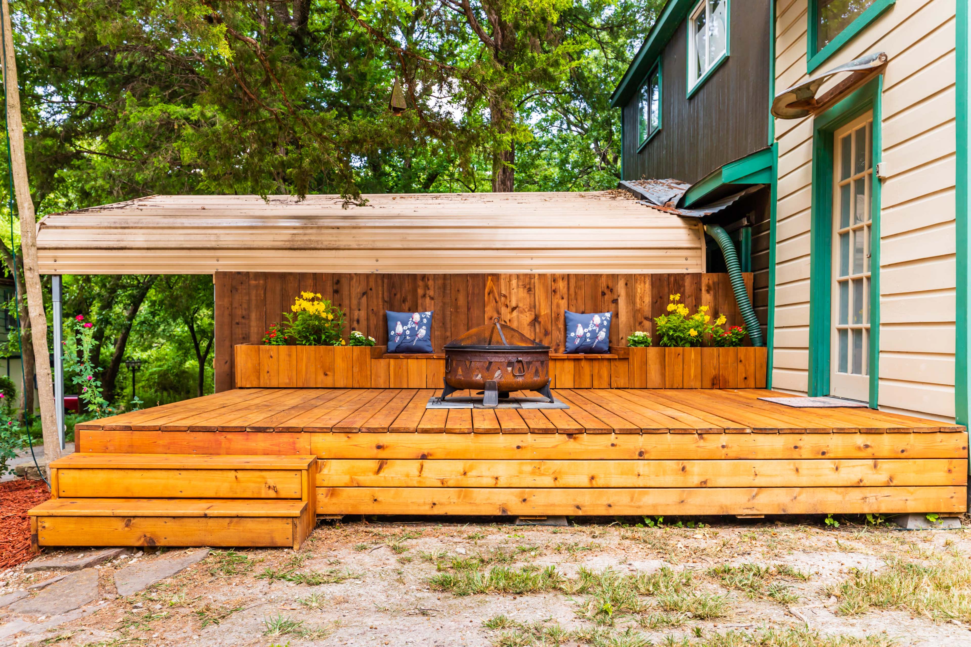 A wooden deck with seating and flower boxes is situated next to a house, featuring a fire pit at the center.