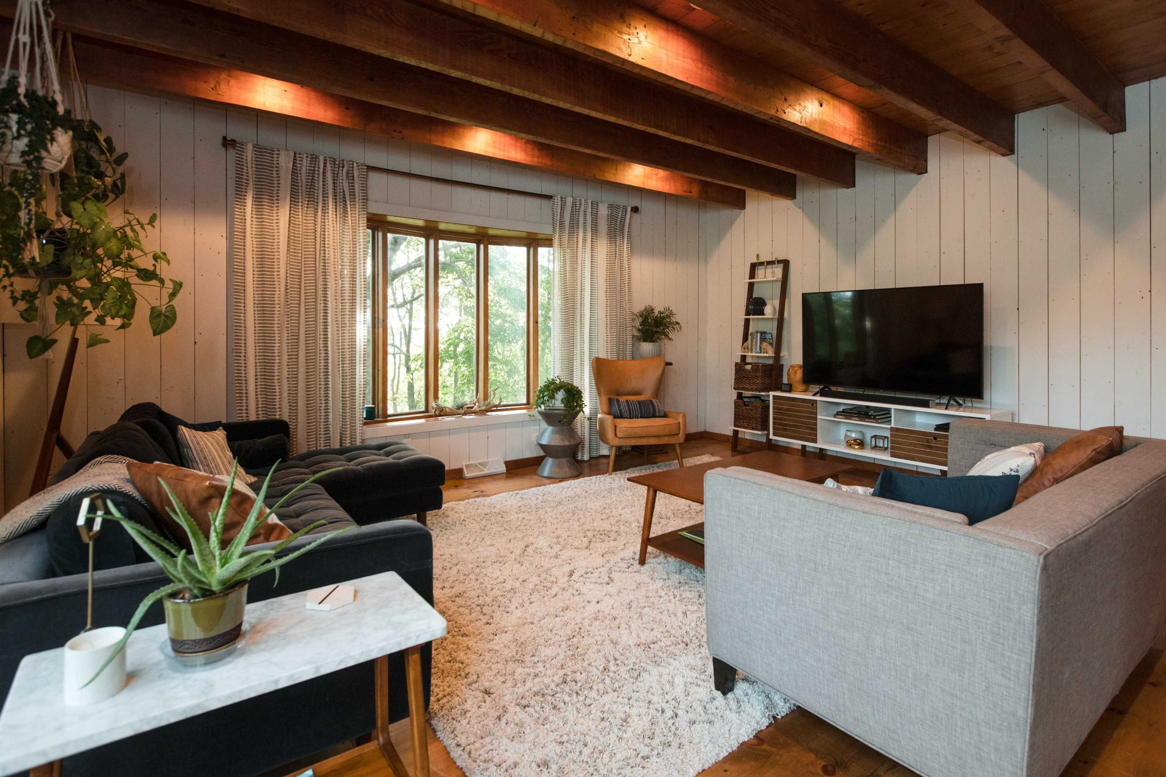 A living room features two sofas, a coffee table, and a large window with greenery visible outside.