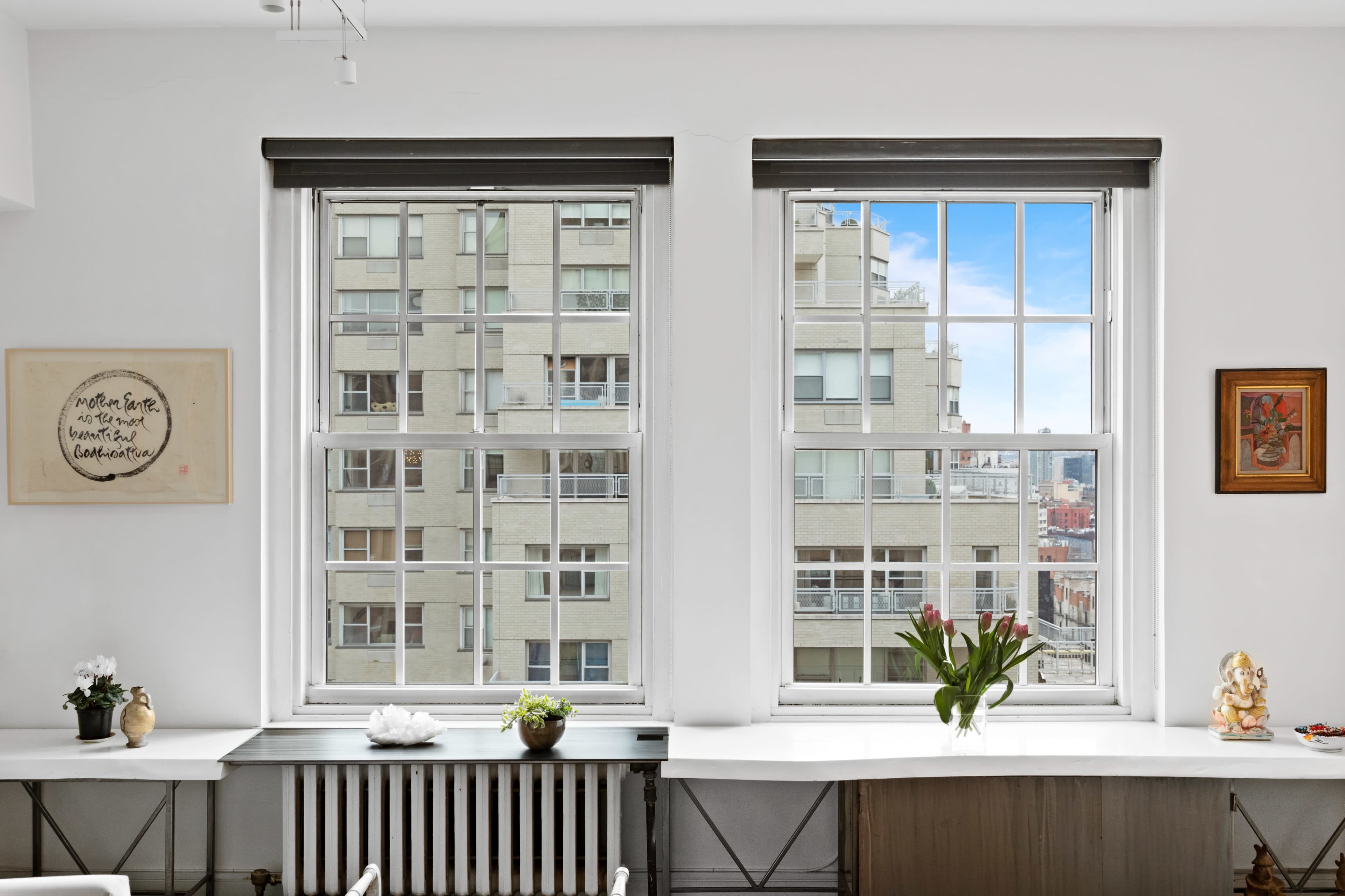 The image shows two large windows with a view of a building across the street, framed by a light interior and decorative items on the windowsill.
