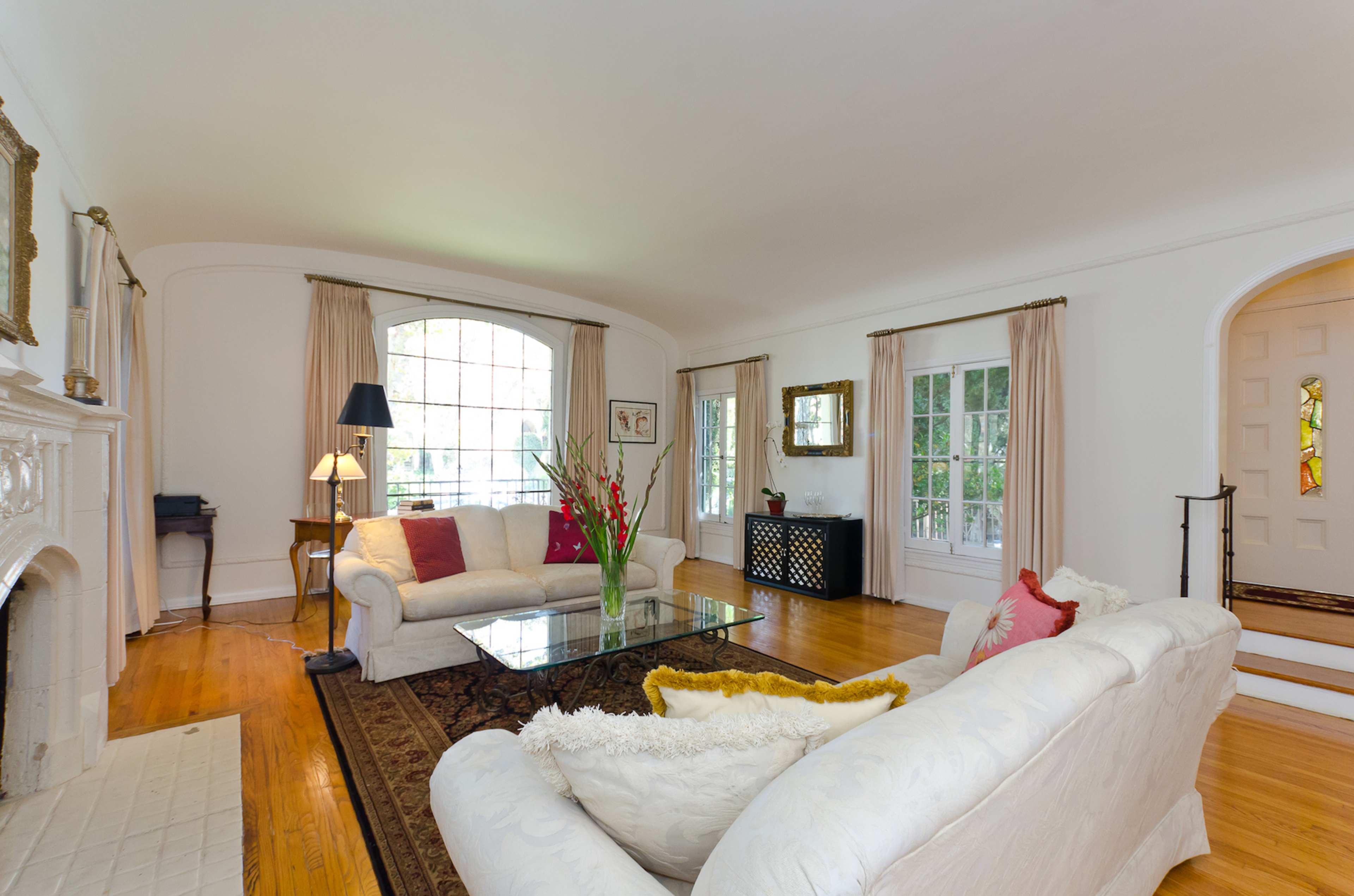 The living room features two sofas, a glass coffee table, and large windows that let in natural light, accented by a fireplace and a decorative entryway.
