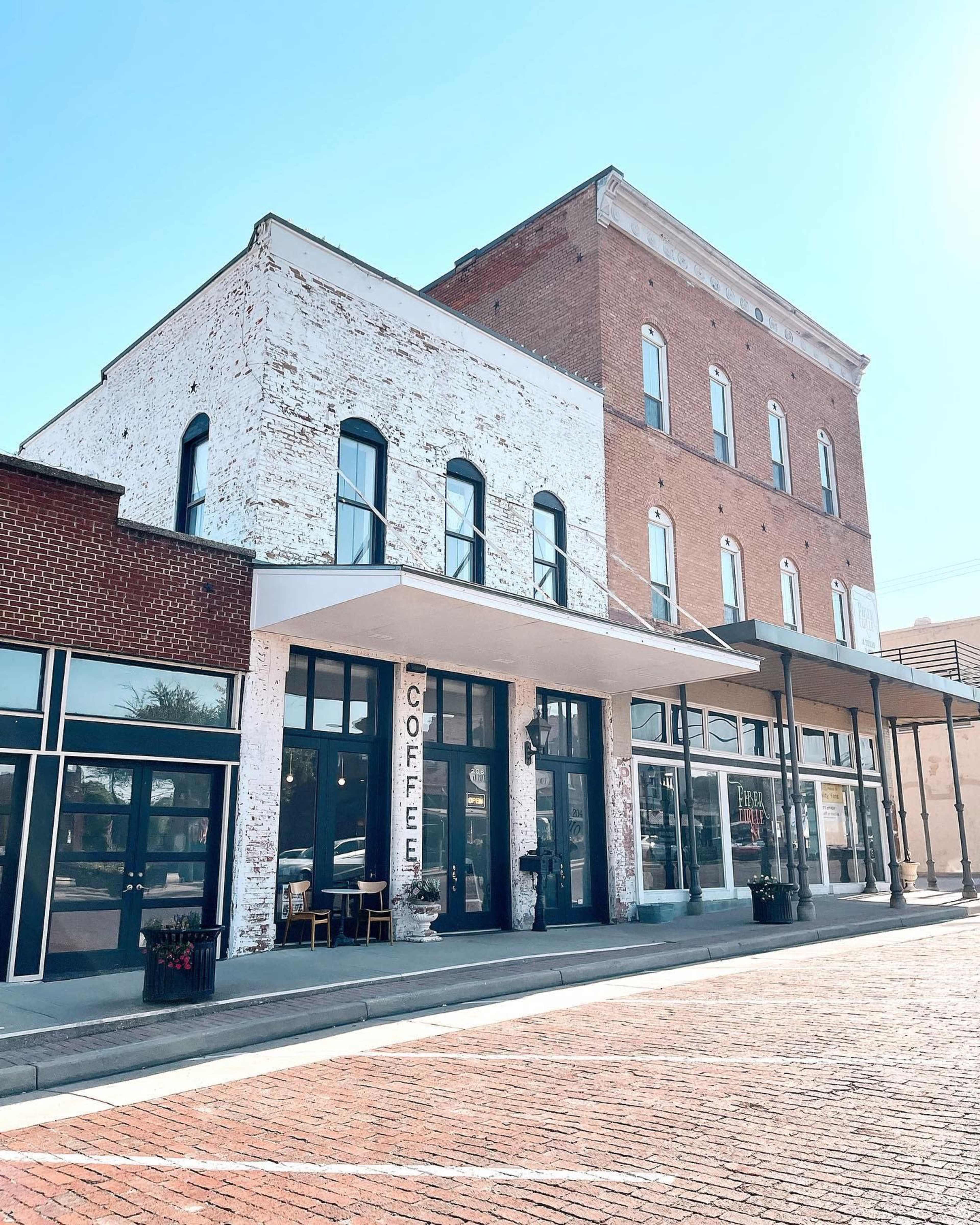 A historic brick building with a whitewashed facade and large windows, featuring a coffee shop on the ground floor.