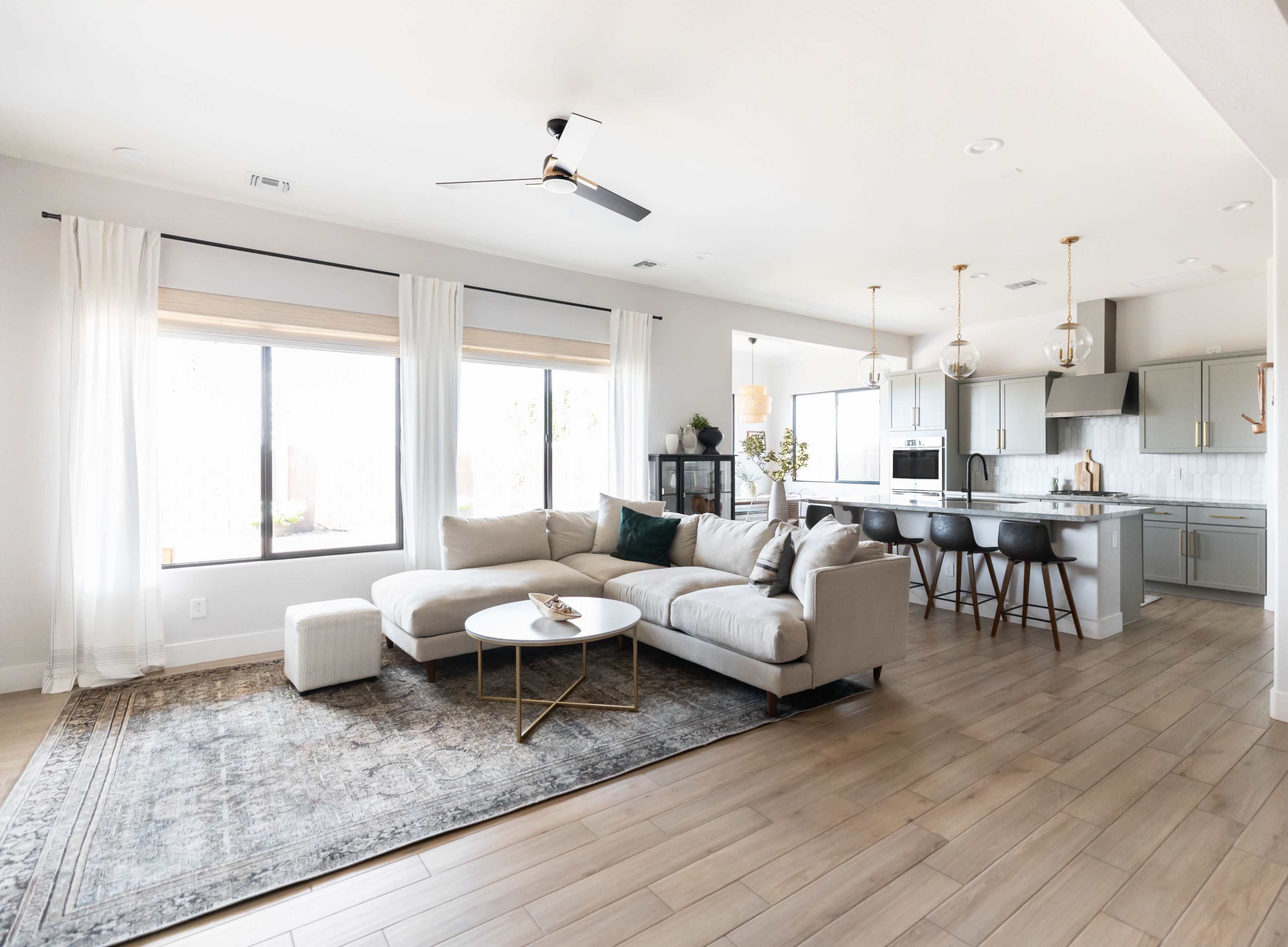 A modern living room features a sectional sofa, a round coffee table, and an open kitchen area with sleek cabinetry and bar stools.