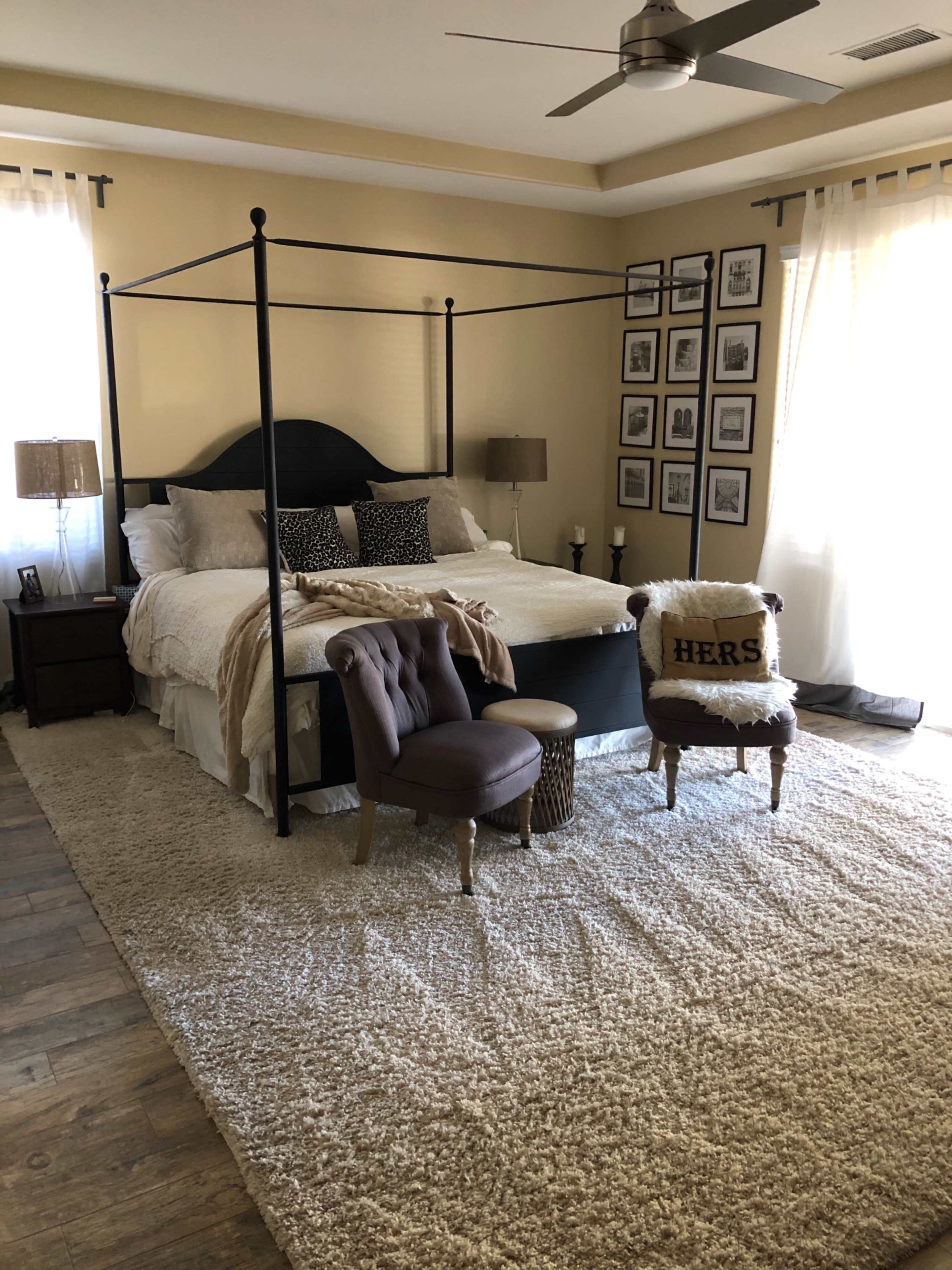 A spacious bedroom featuring a four-poster bed, two bedside tables, and a cozy seating area with a chair and small table on a plush carpet.