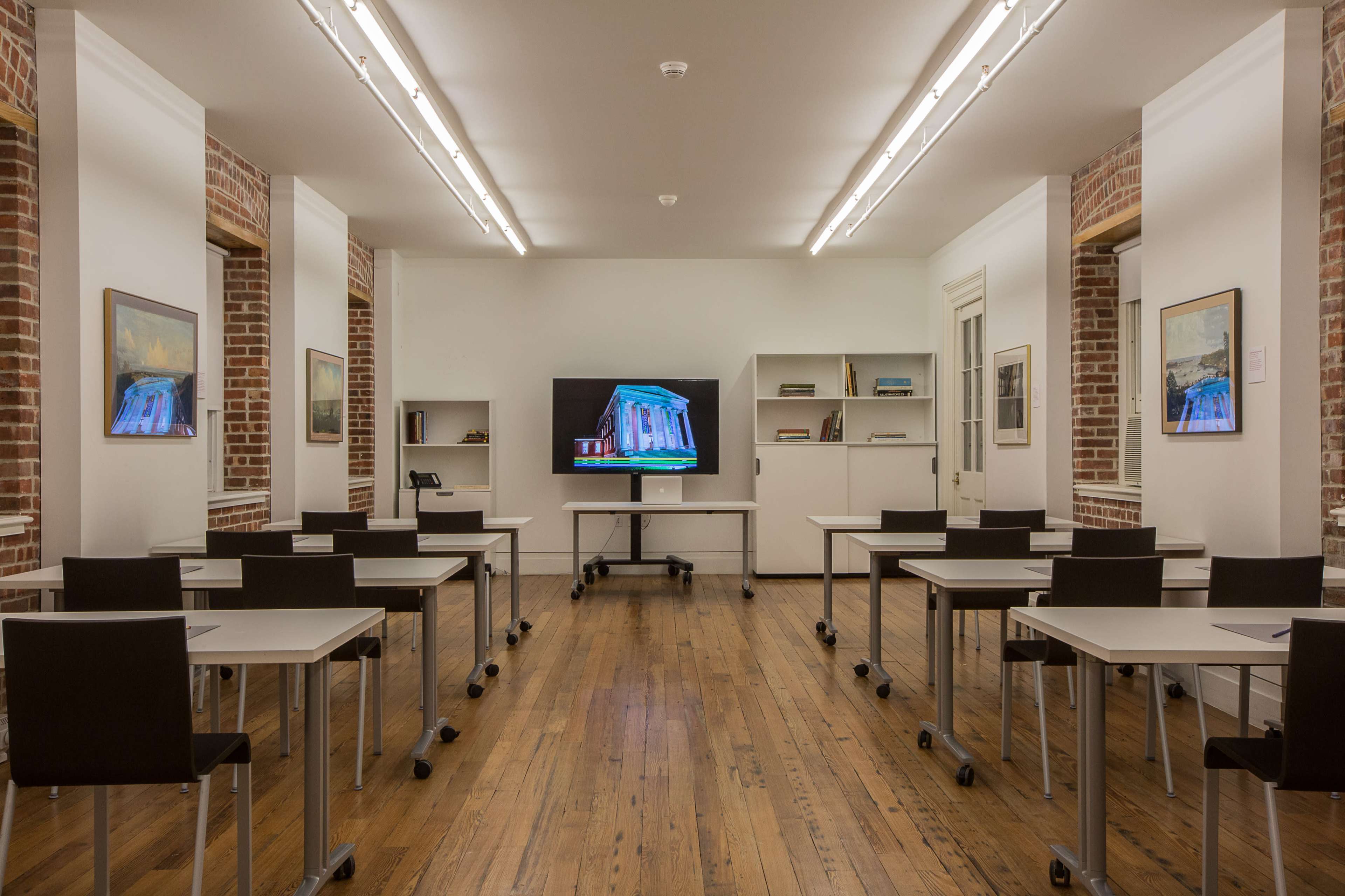 A well-lit classroom with rows of modern desks and a large screen at the front, surrounded by brick walls and shelves.