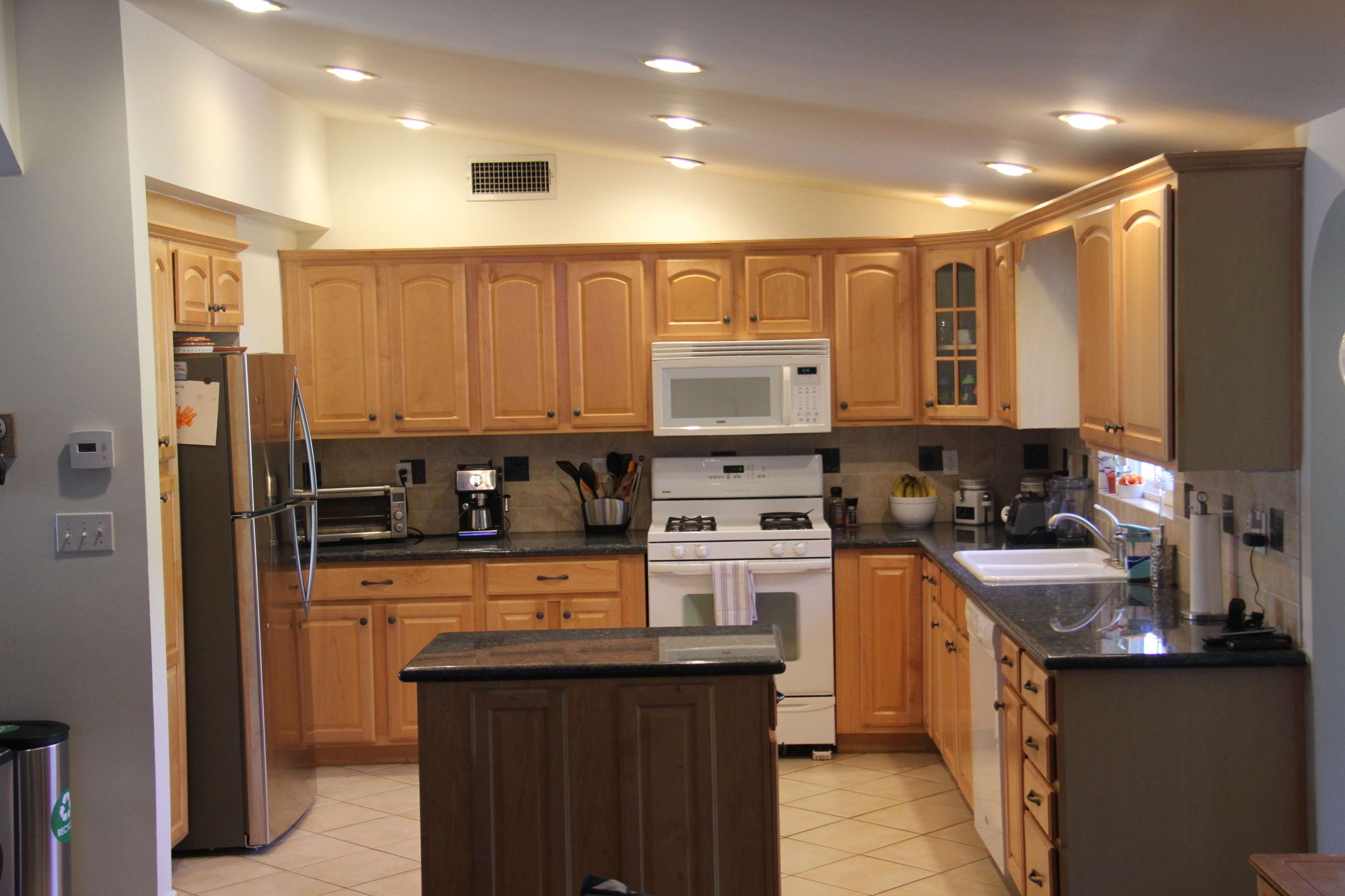 A modern kitchen with wooden cabinets, a stainless steel refrigerator, a white stove, and a counter with various kitchen appliances.