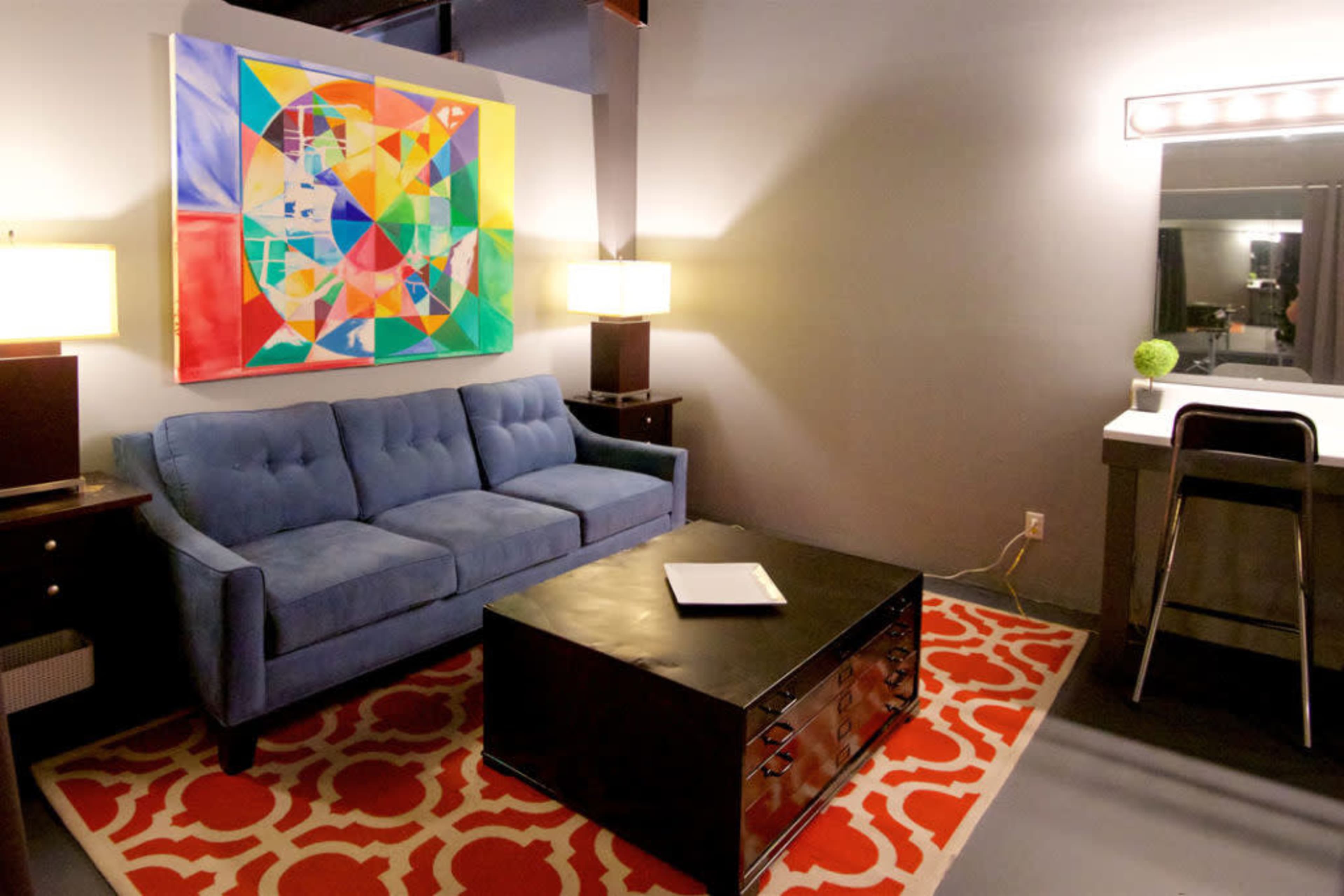 A modern living area featuring a blue couch, a black coffee table, and an abstract painting on the wall, complemented by a red and white patterned rug.