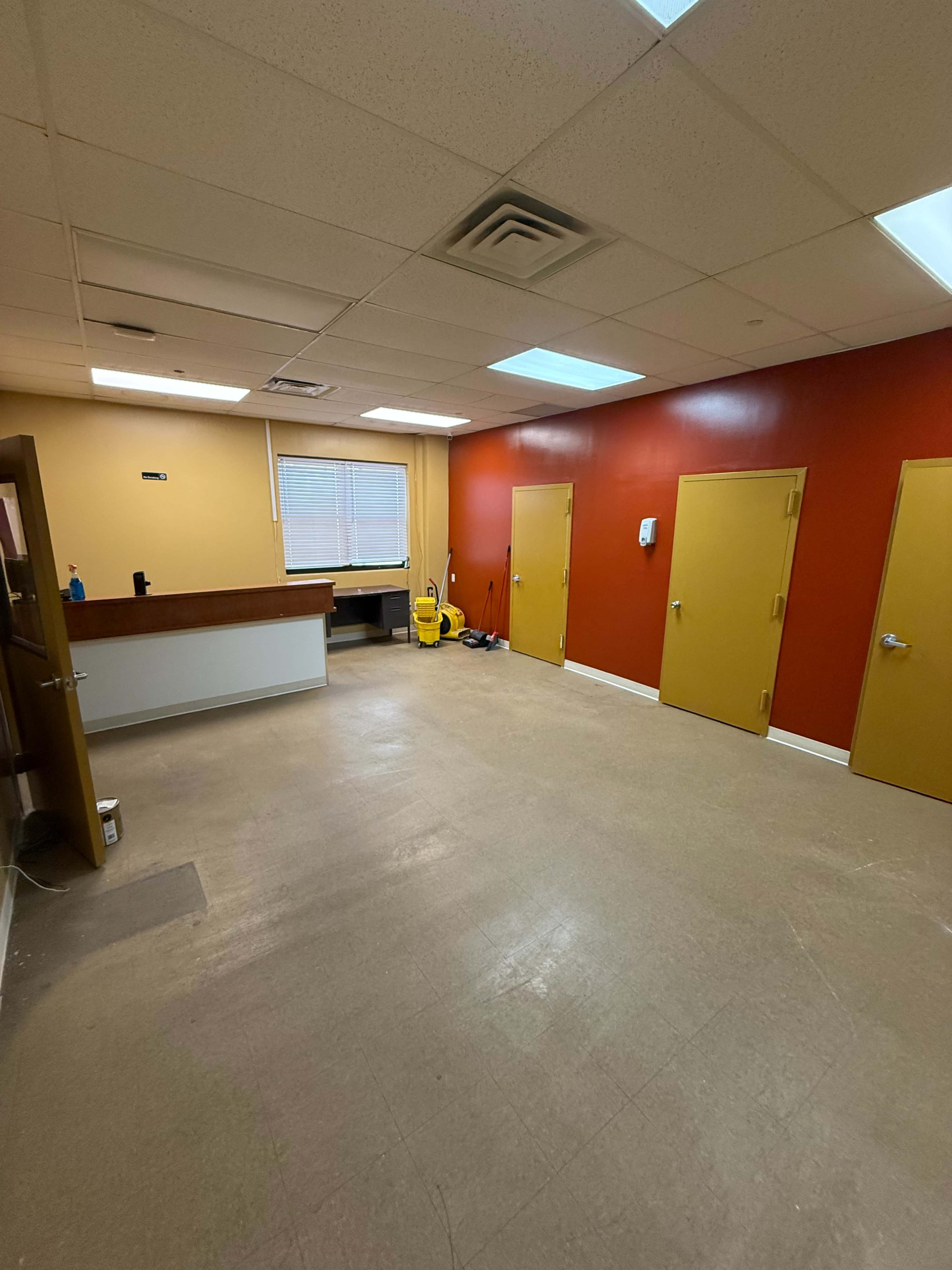The image shows a vacant room with a reception area and multiple colored doors along the walls.