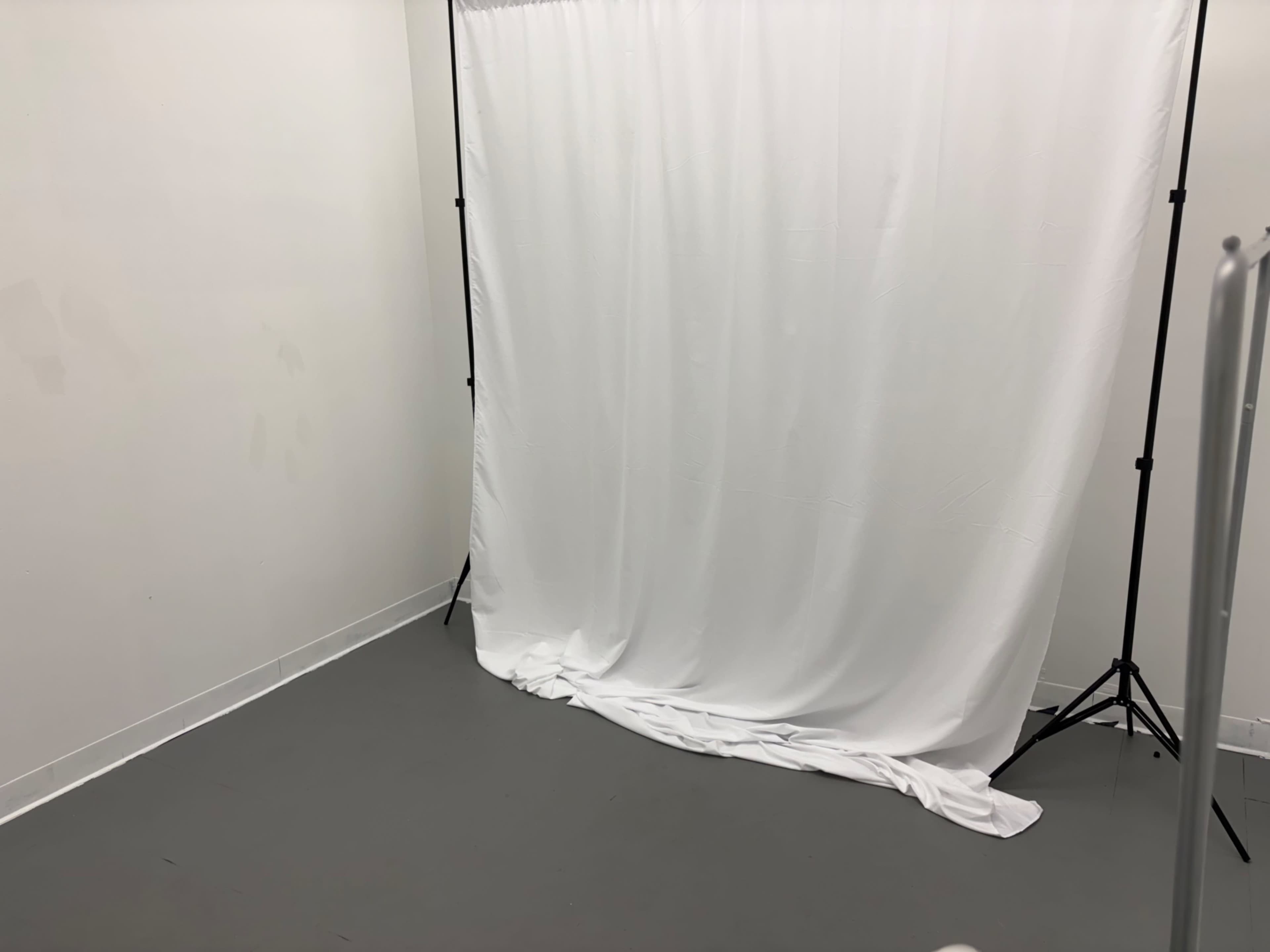 The image shows a bare room with a white backdrop draped on a support frame, set against a plain wall and gray floor.