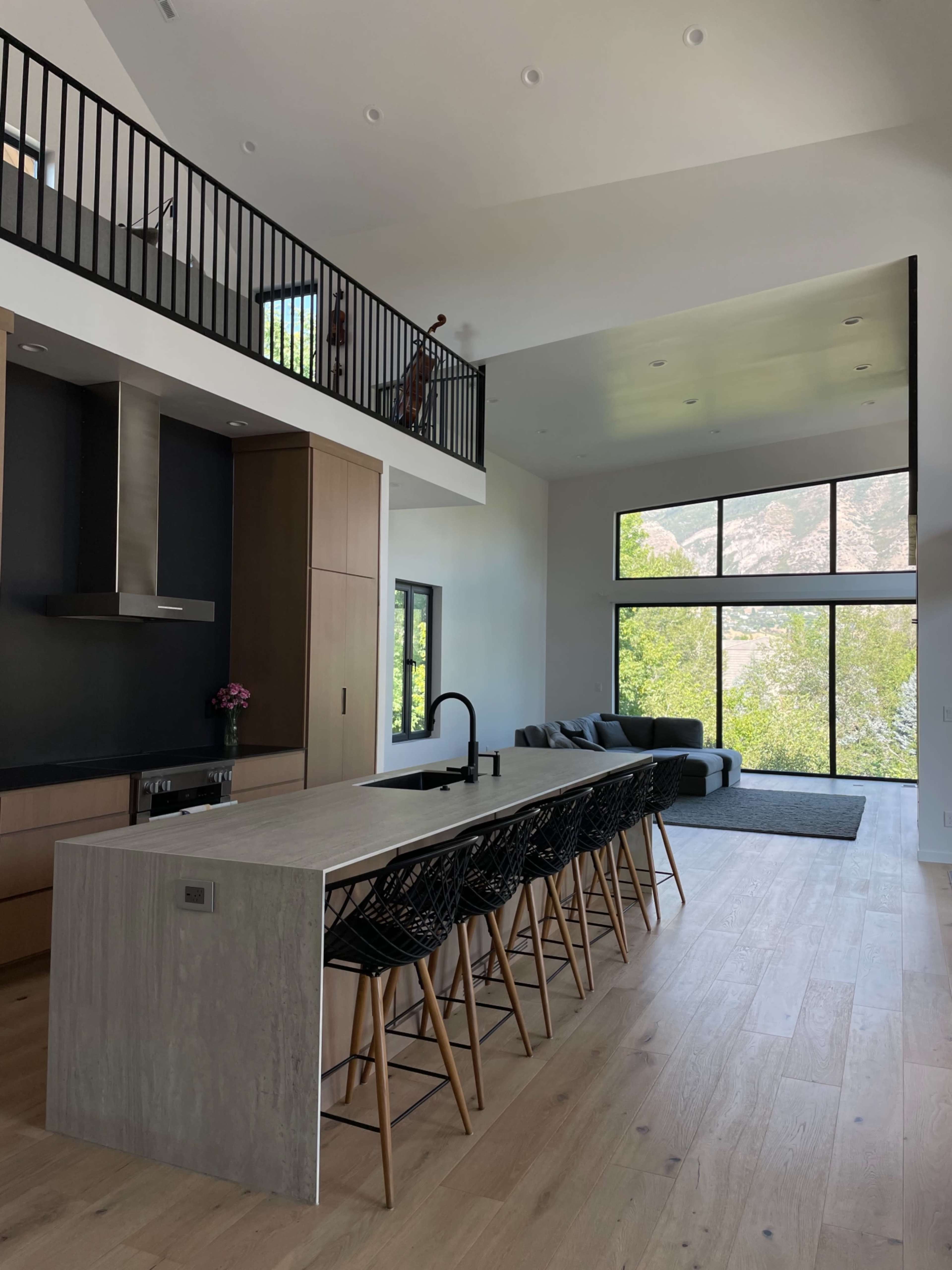 A modern kitchen features a large island with bar seating, overlooking a spacious living area with large windows and a view of the outdoors.