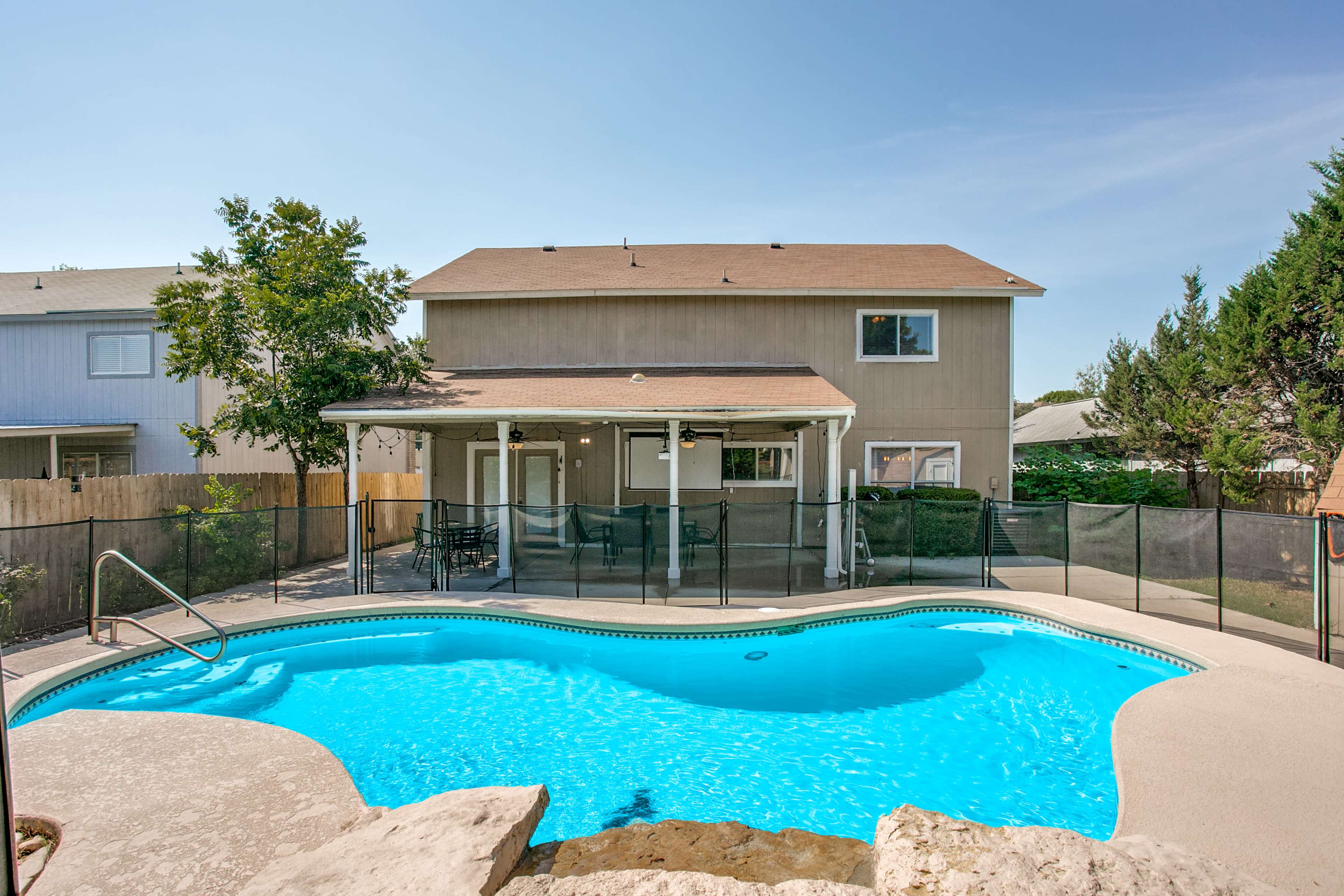A swimming pool is located in the foreground with a fenced patio and a two-story house visible in the background.