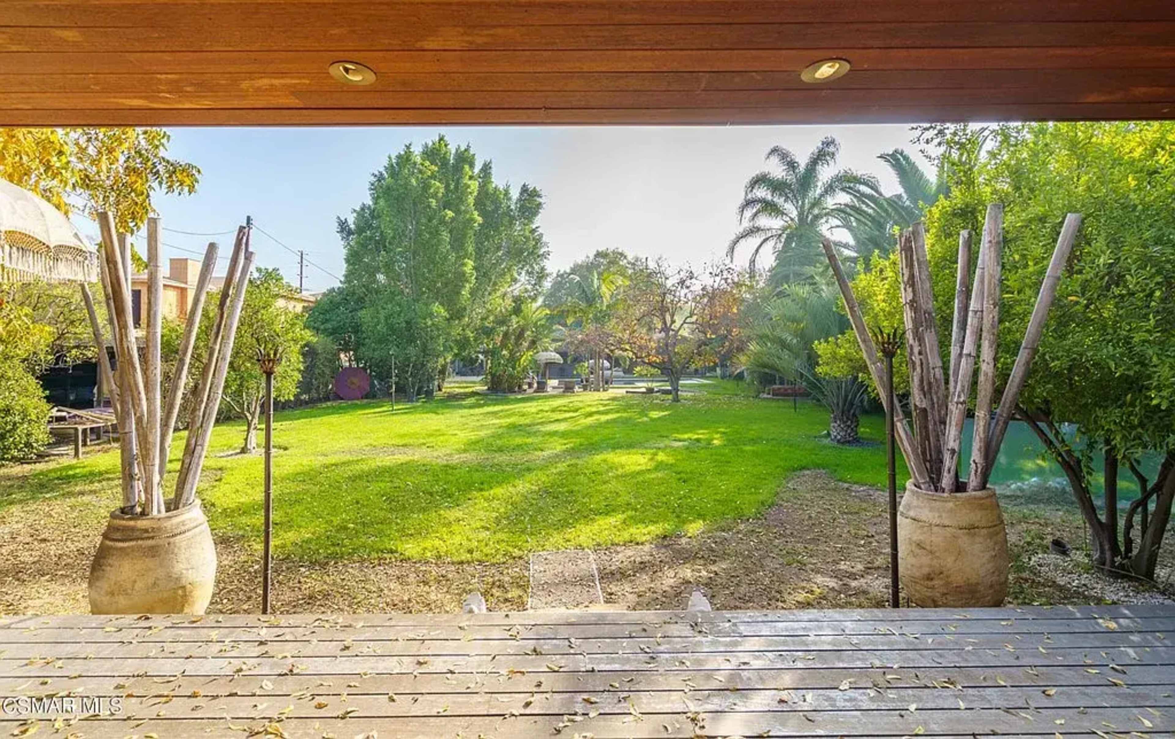 The image shows a view of a spacious garden with green grass and various trees framed by a wooden structure.