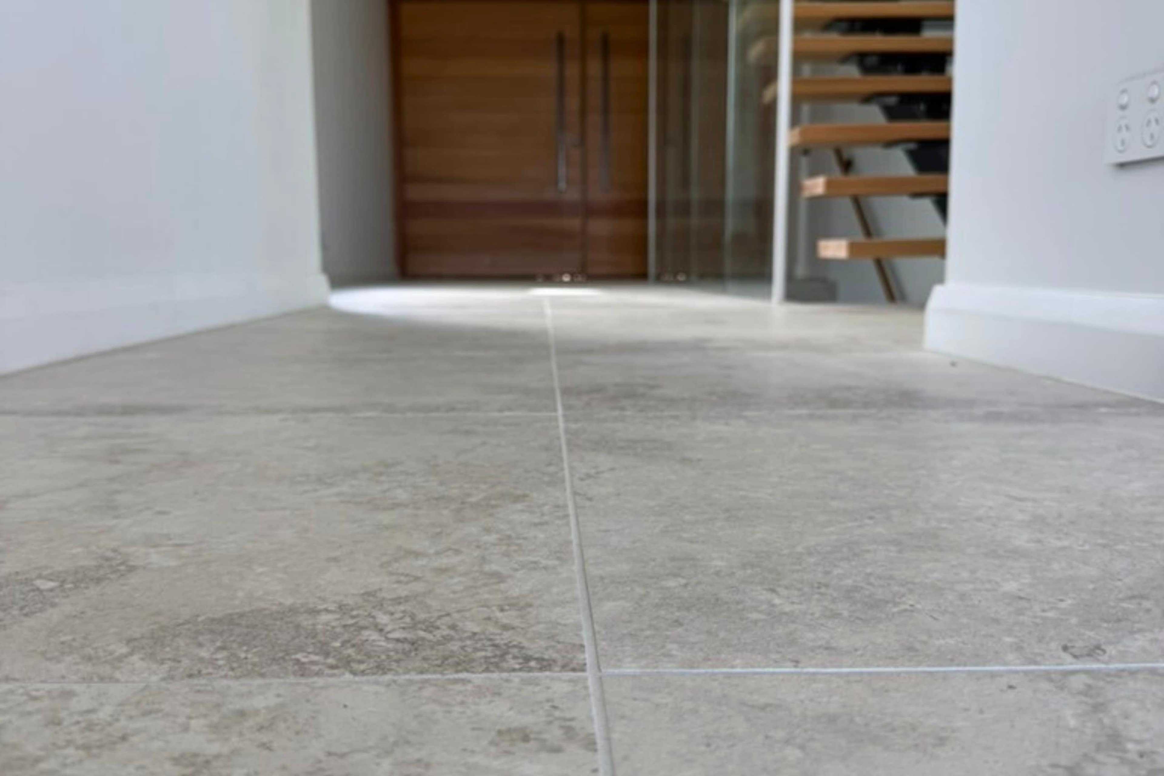 A tiled hallway leads to a wooden door partially visible at the end, with a staircase on the right side.