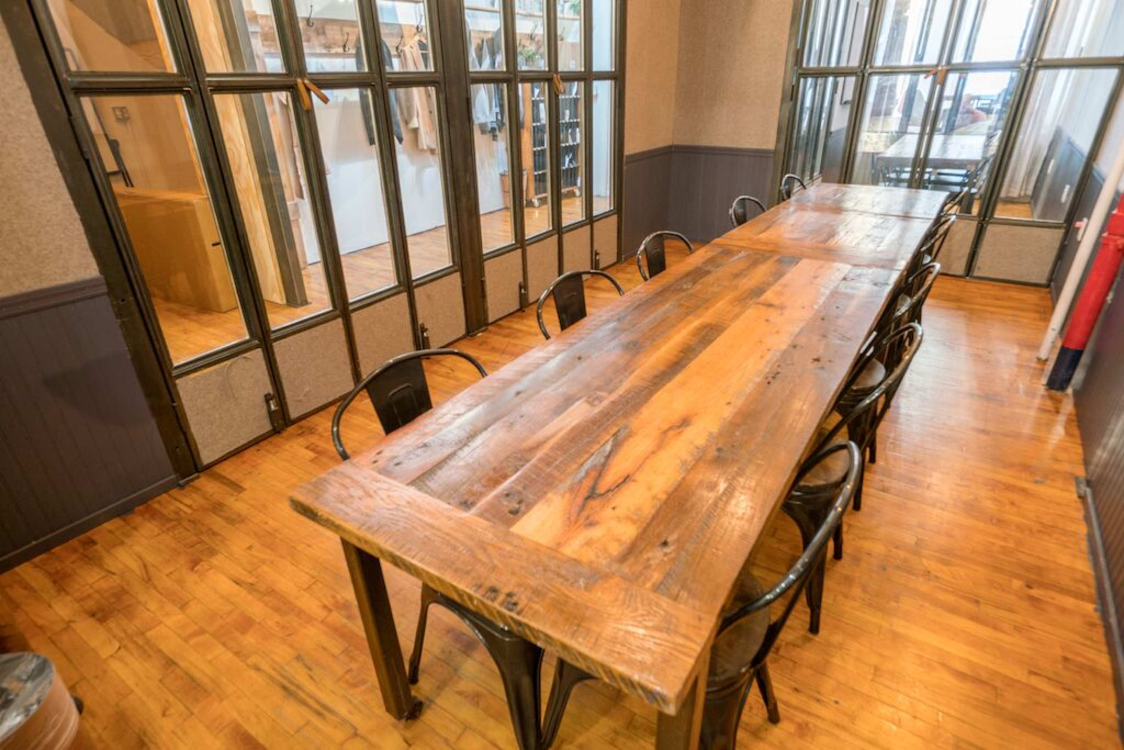 A long wooden table with metal chairs is arranged in a room with large glass-paneled walls.