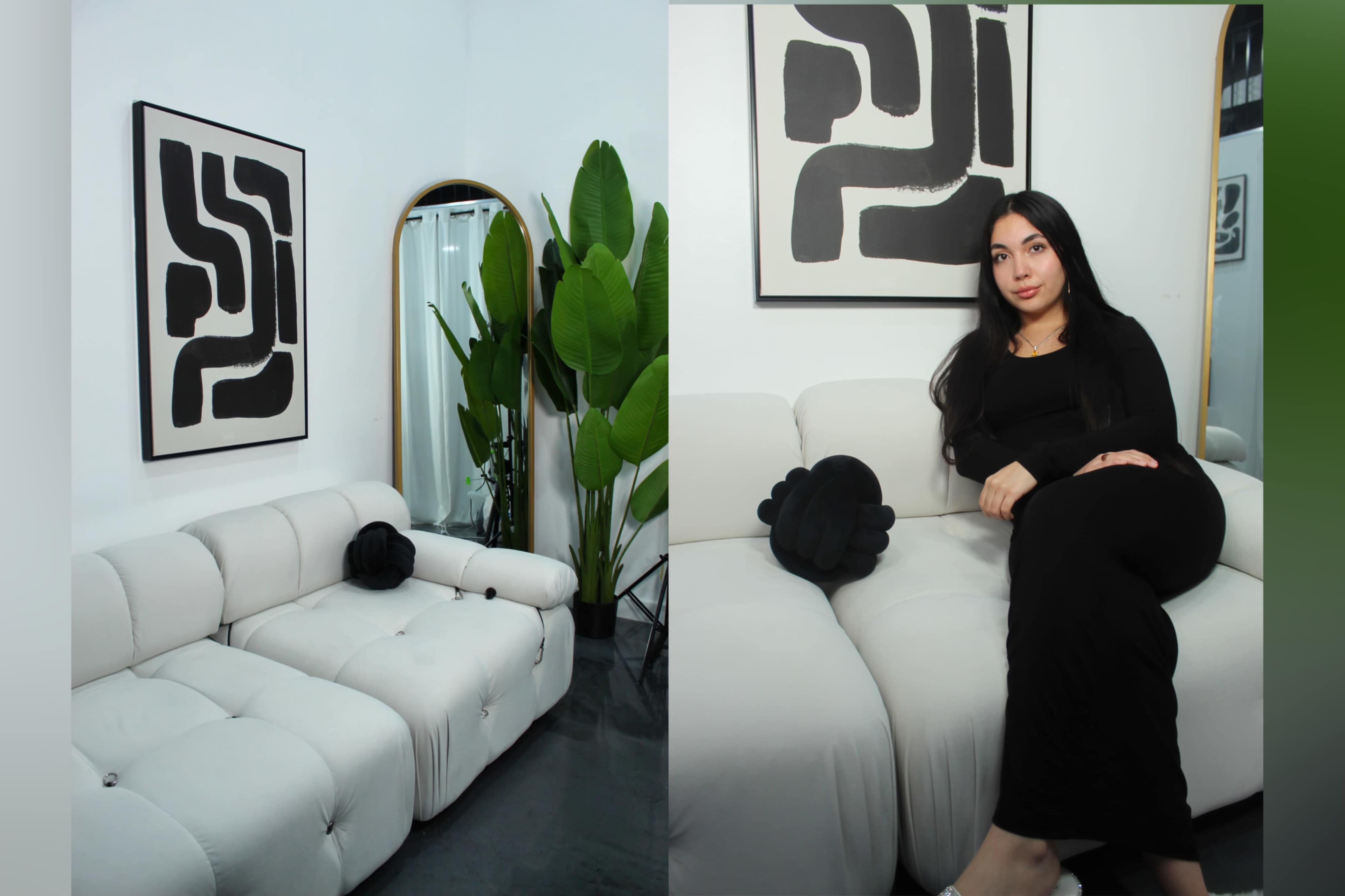 A woman sits on a white sofa in a modern room adorned with a large abstract black and white artwork and leafy plants.