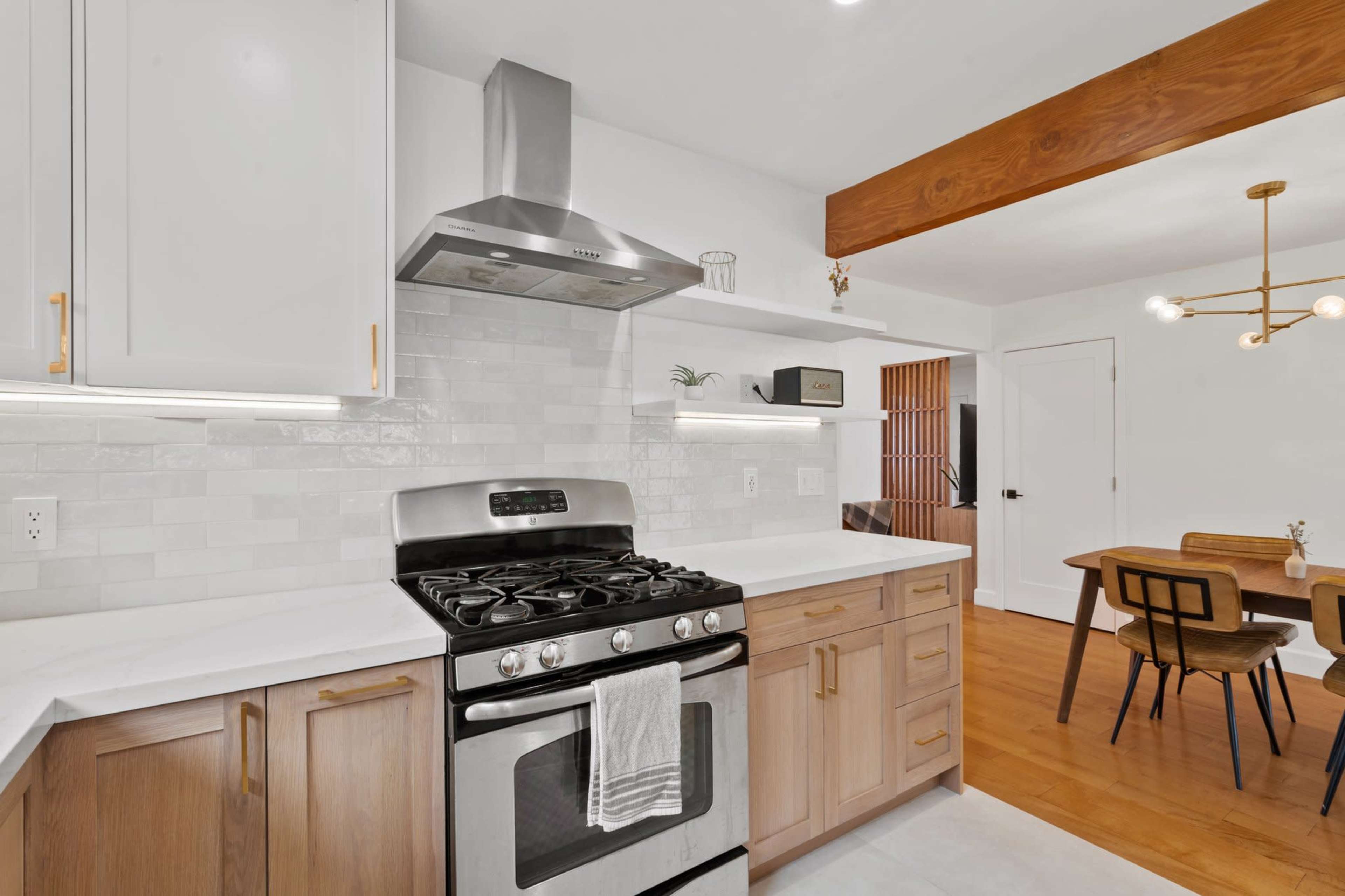 A modern kitchen features a stainless steel gas stove, light wood cabinets, and a dining area with a wooden table and chairs.