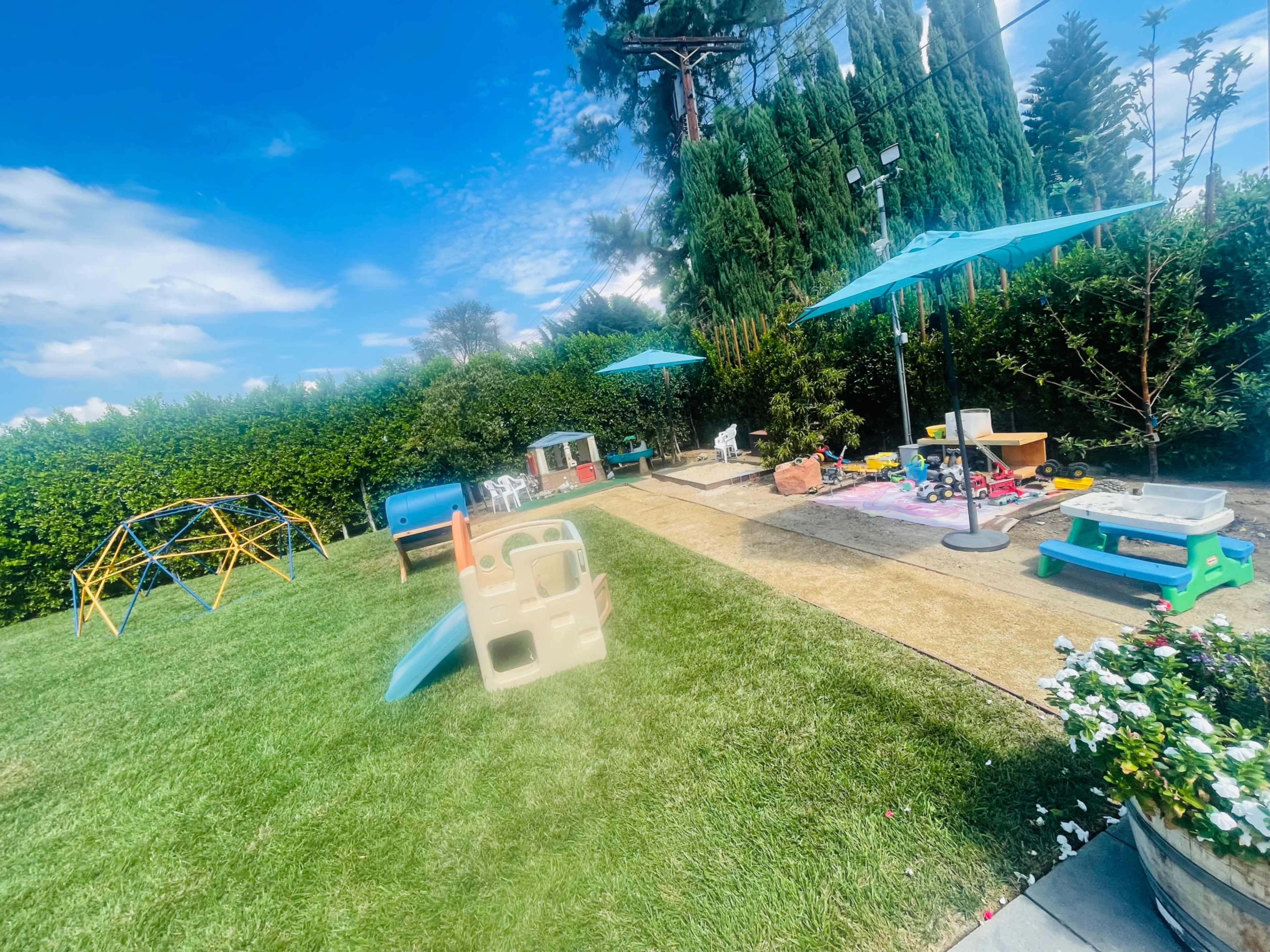 A grassy backyard with play structures, umbrellas, and several outdoor toys.