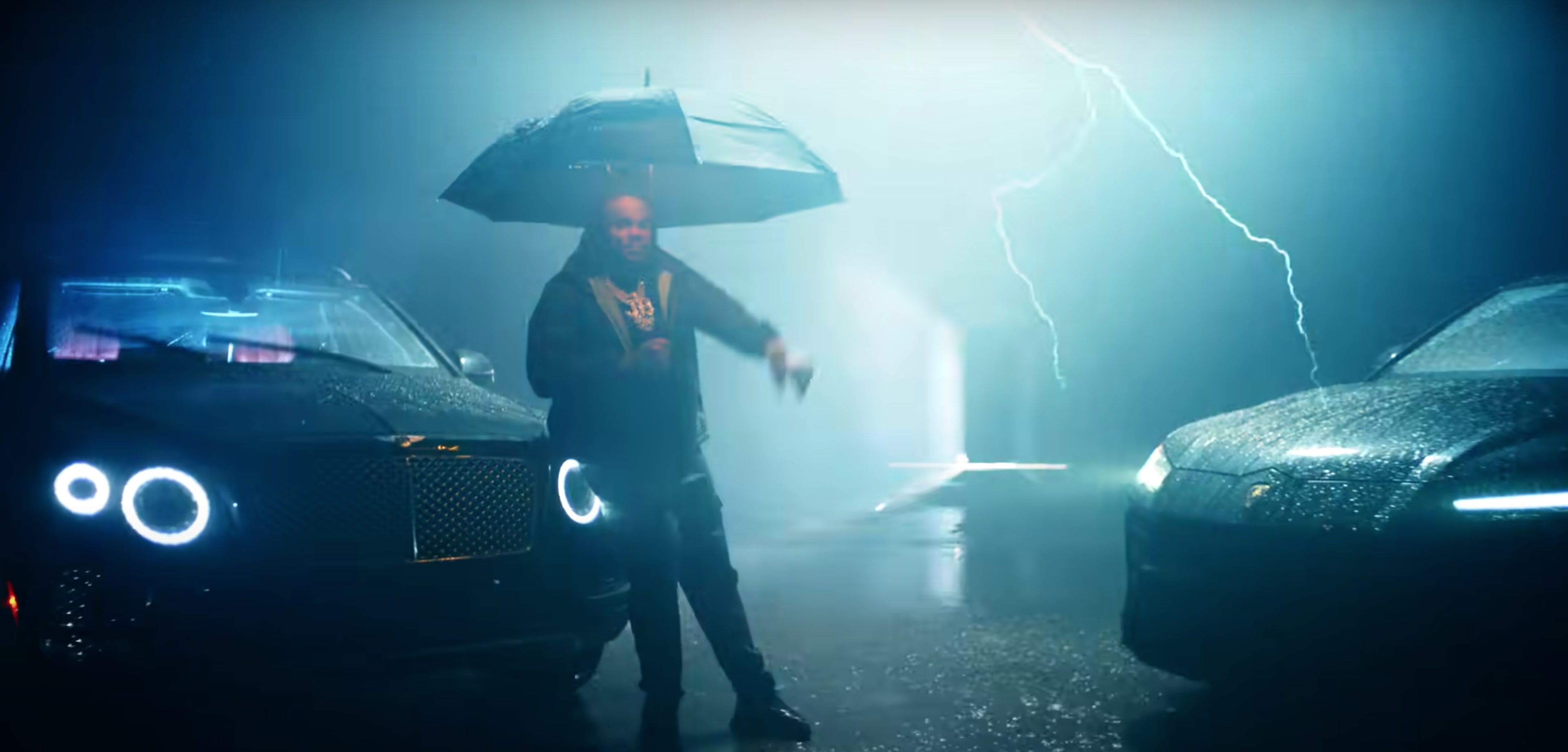 A person holding an umbrella stands between two luxury cars in a rainy, illuminated setting with lightning in the background.