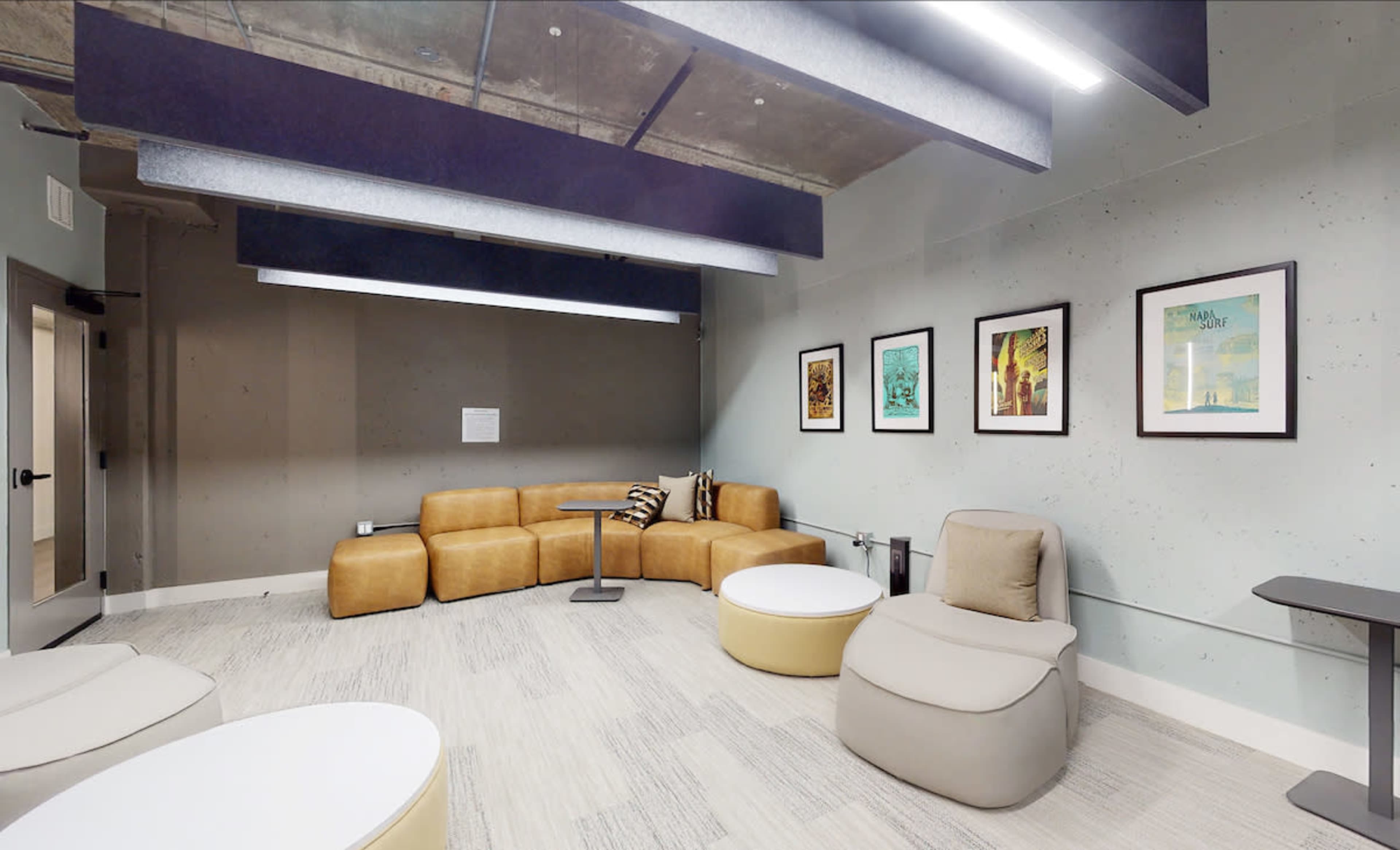 A modern lounge area featuring a curved brown couch, two light-colored round tables, and several framed artworks on the walls.