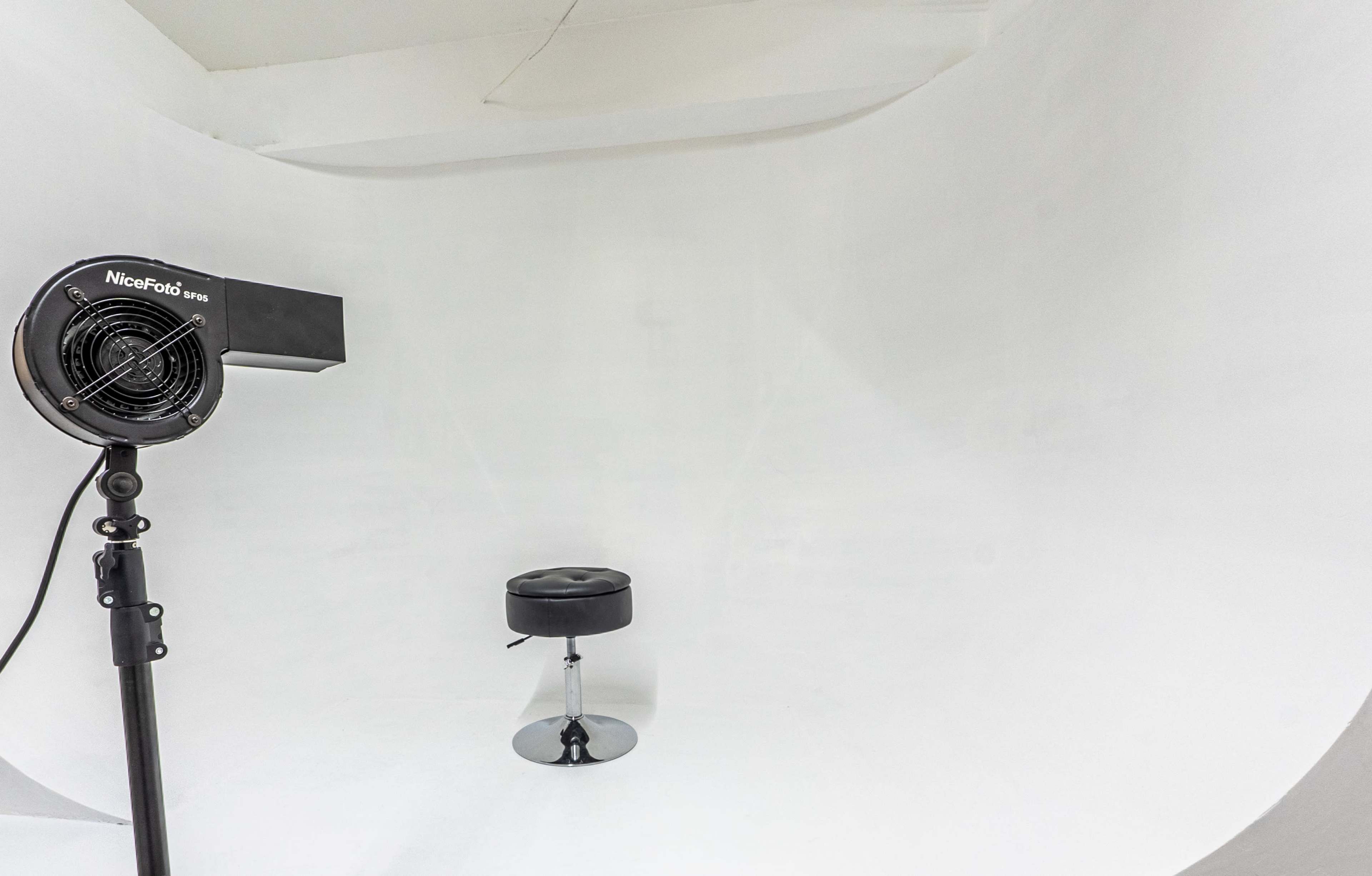 A photography setup with a black fan positioned beside a shiny chrome stool against a white backdrop.