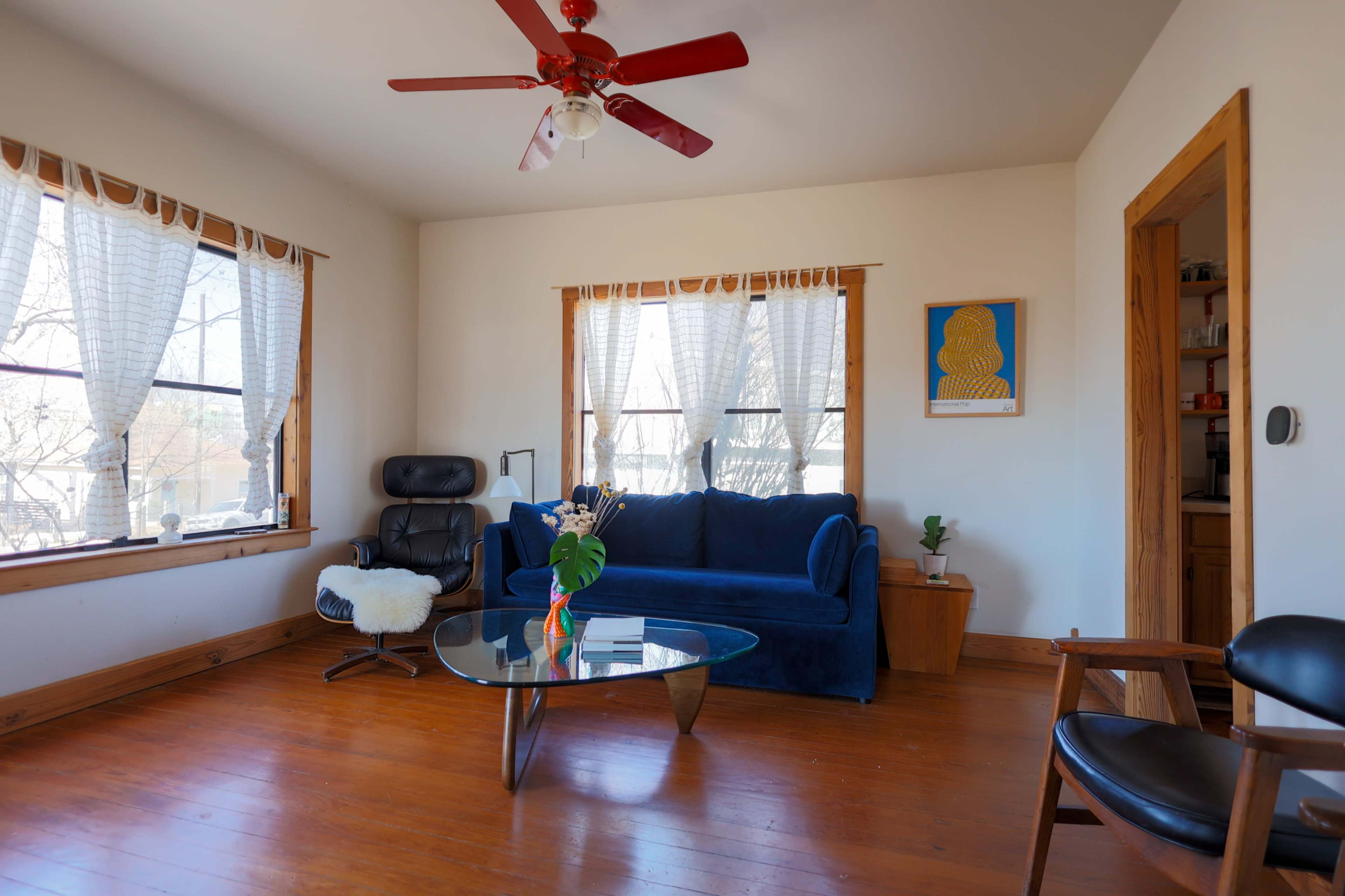 The room features a blue couch, a glass coffee table, and a small plant, illuminated by natural light through the windows.