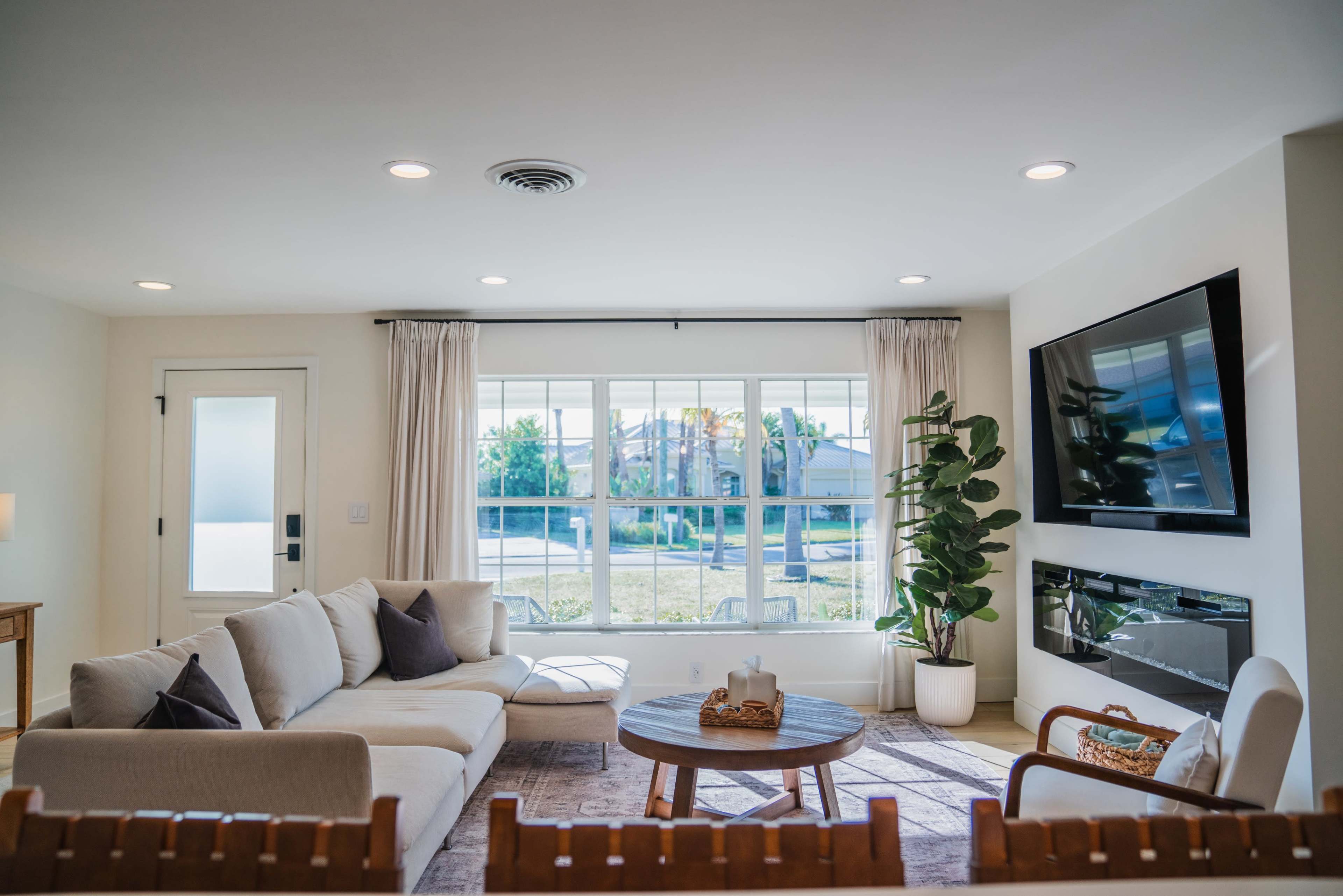 The living room features a sectional sofa, a coffee table, and a large window overlooking a landscaped area.