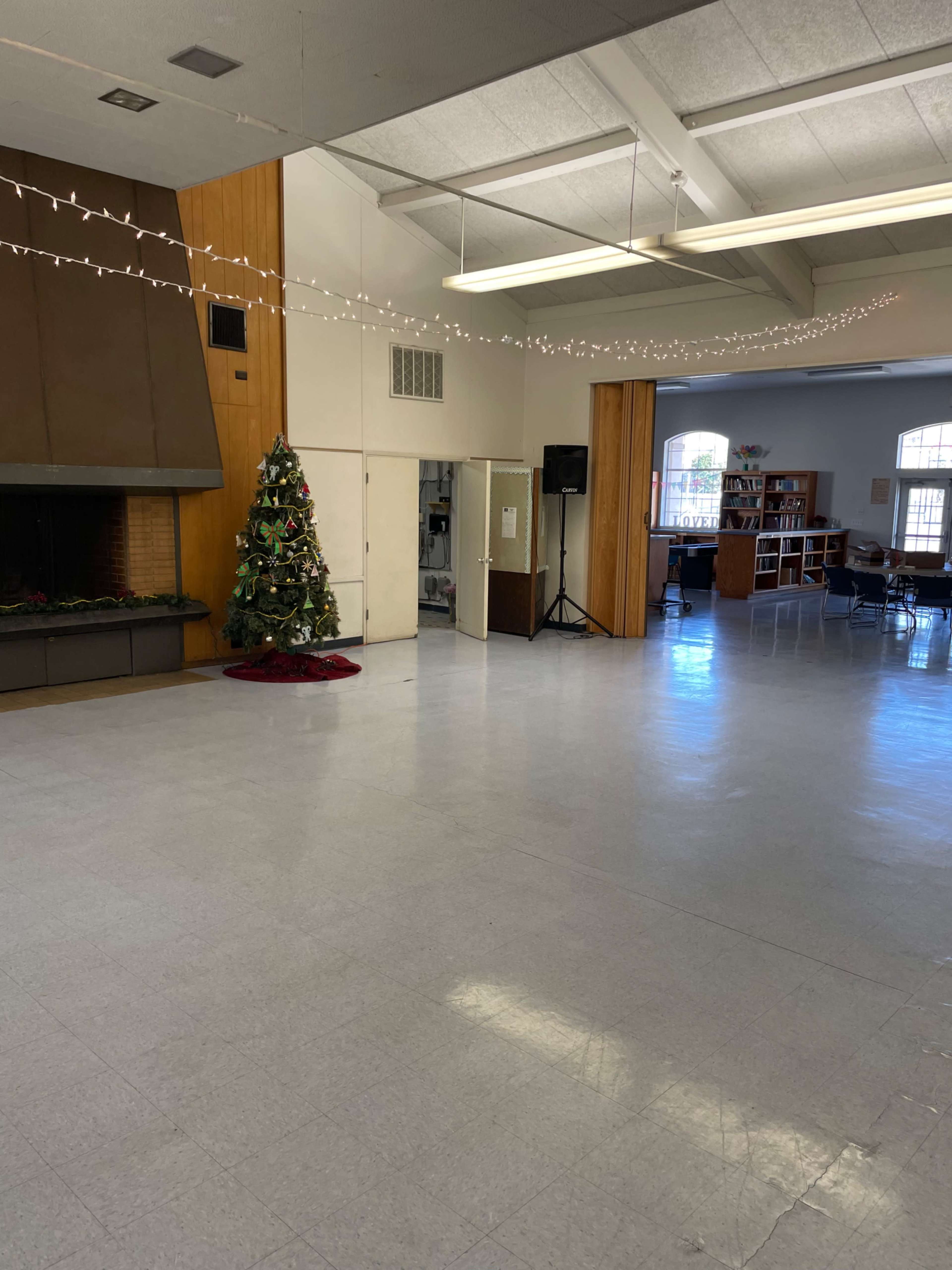 A large, empty room with a fireplace, a Christmas tree in the corner, and a doorway leading to another area.