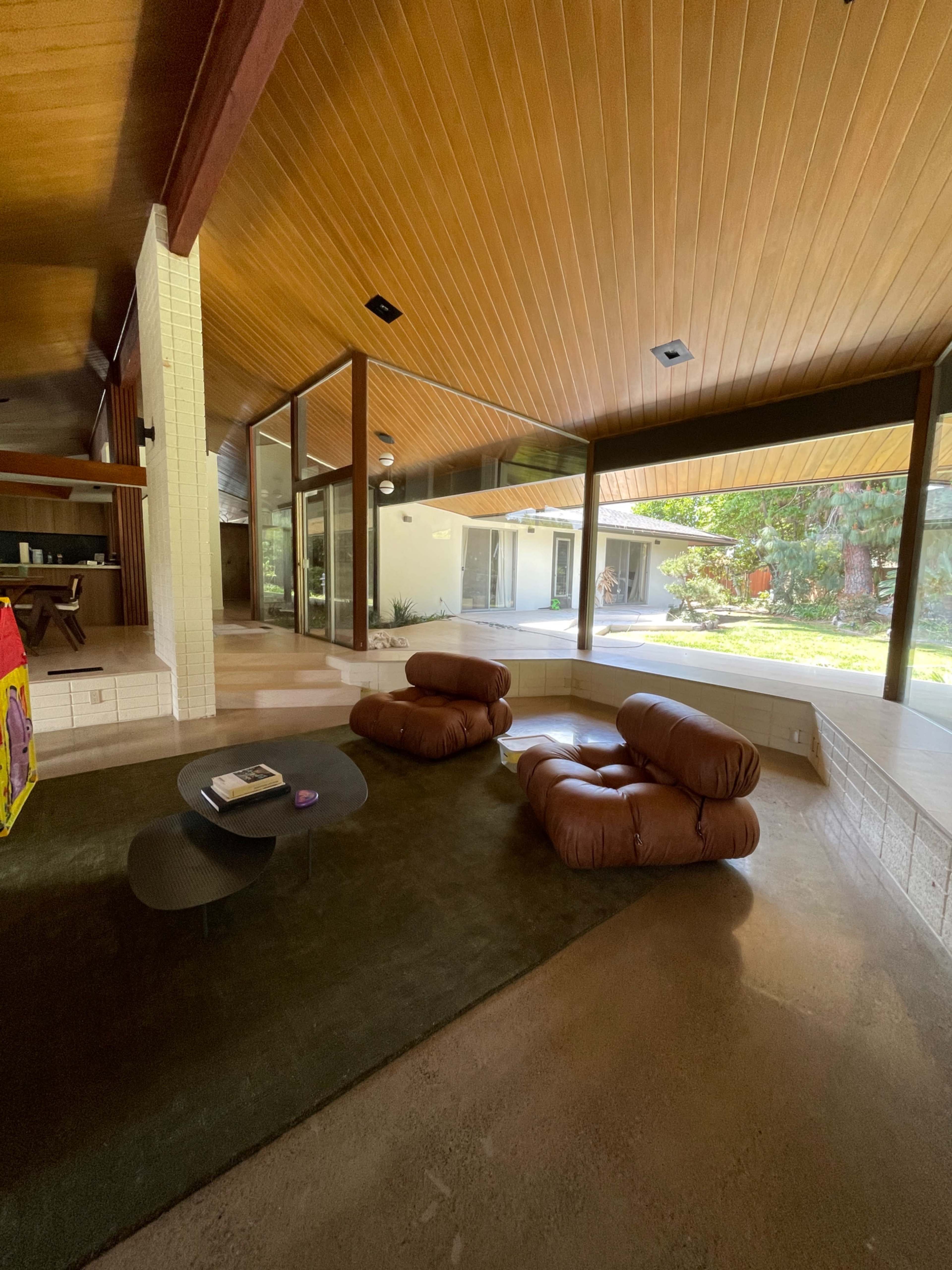 A modern living room featuring two brown lounge chairs, a black coffee table, and large windows that provide a view of a grassy outdoor area.