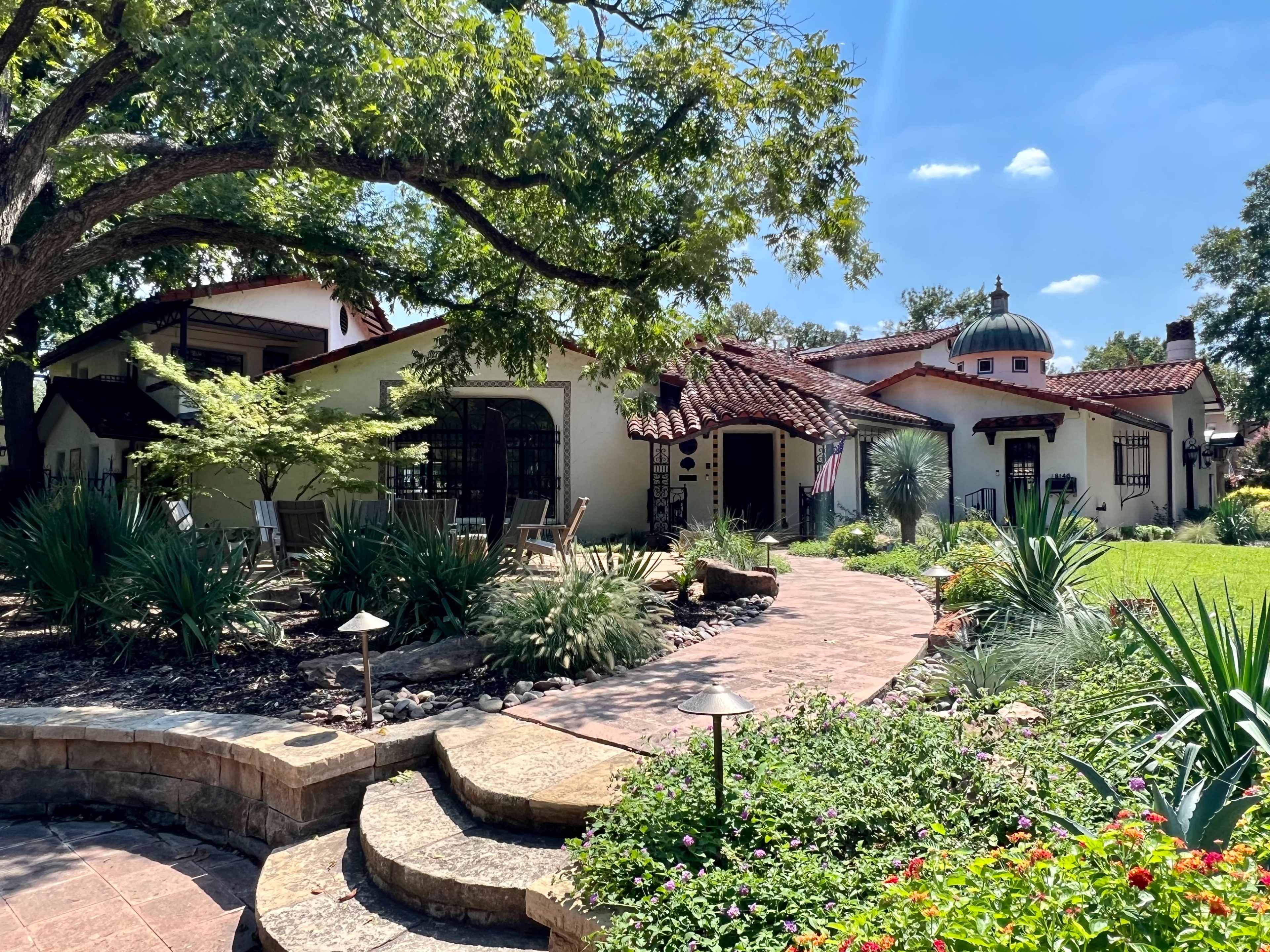 A landscaped garden leading to a Spanish-style home with a domed roof and multiple architectural details.