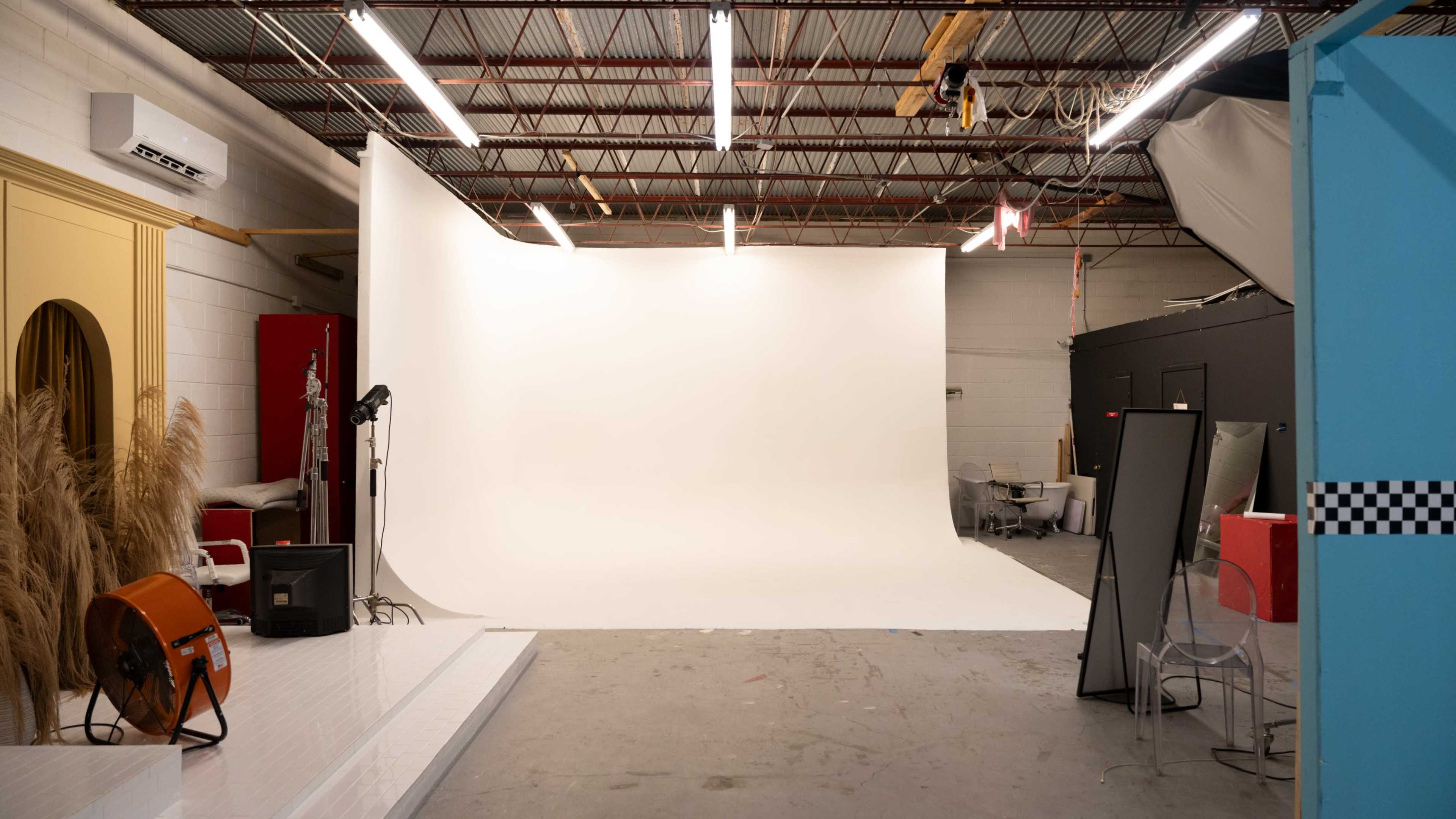 A photography studio with a white backdrop, lighting equipment, and scattered props and furniture.