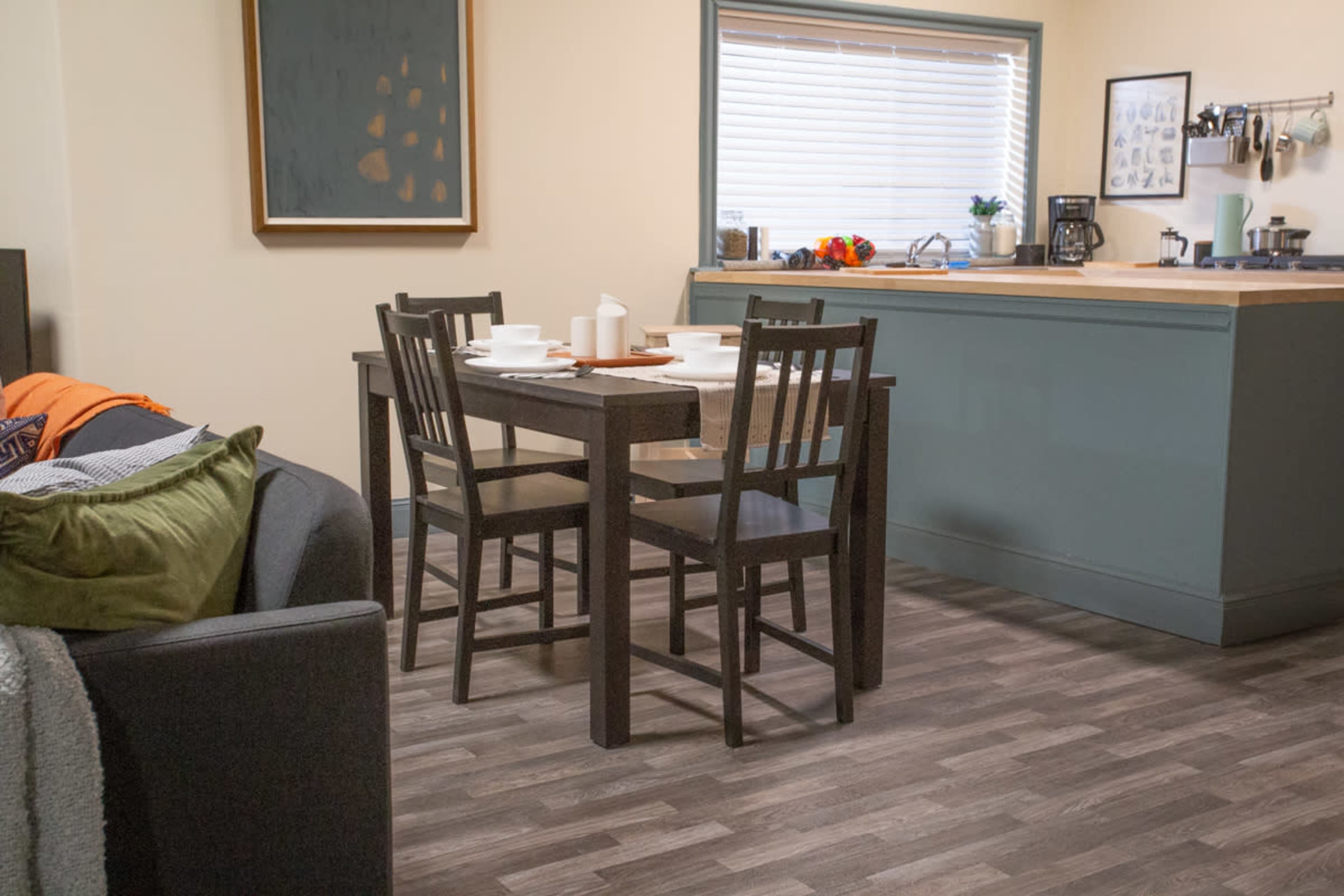 A dining table with four chairs is set in a cozy kitchen area, adjacent to a couch and featuring modern appliances.