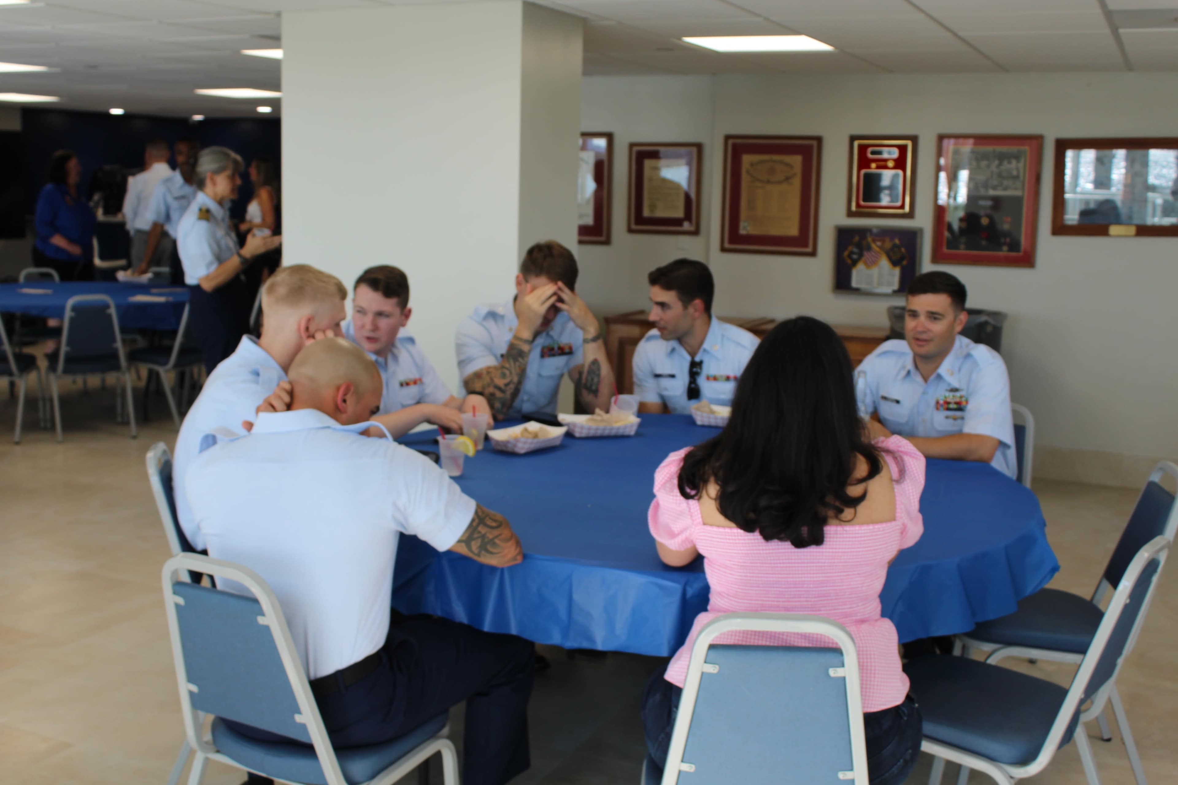 A group of service members and one woman sit around a blue table in a casual dining area, engaged in conversation.