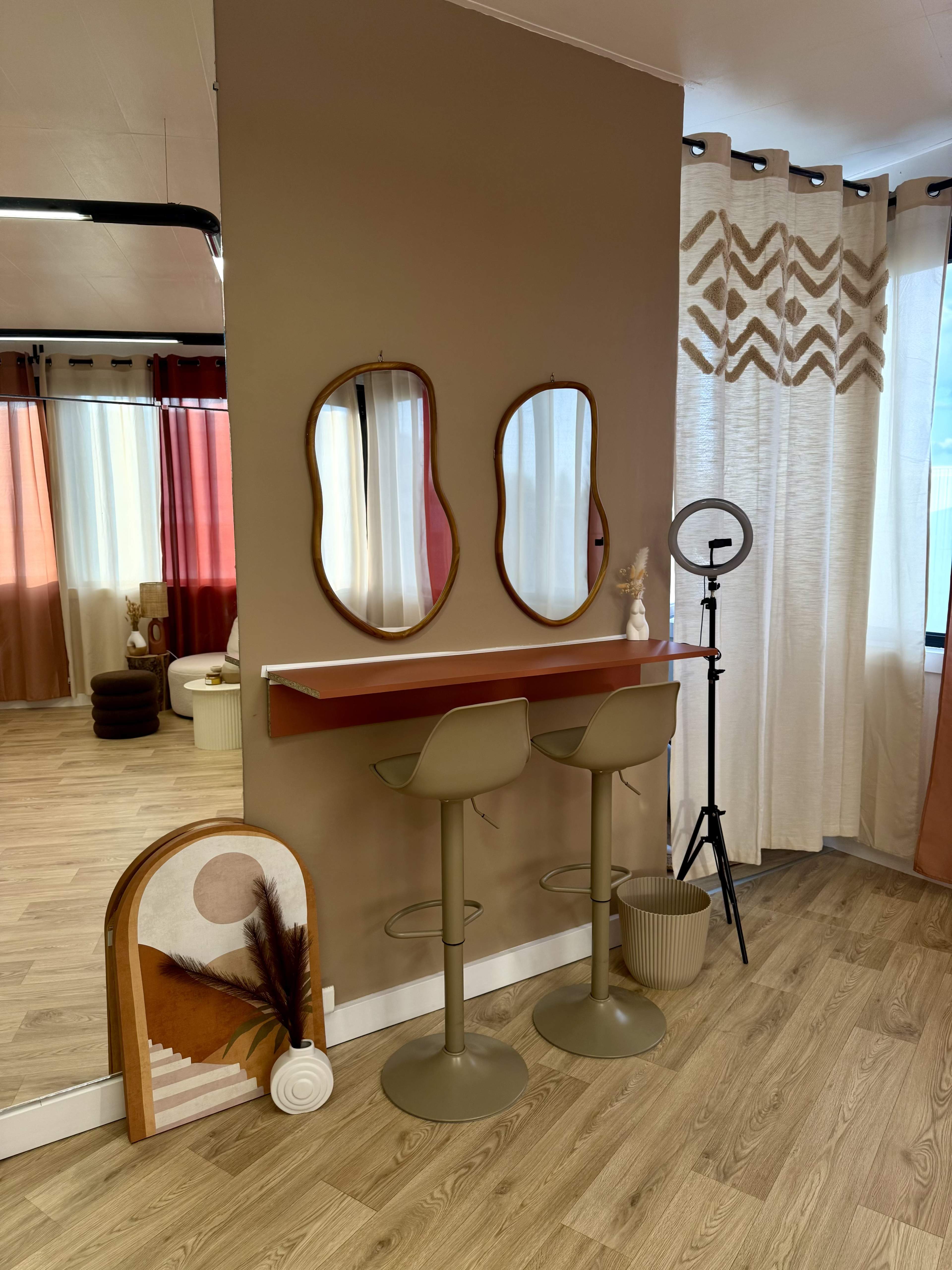 The image features a modern interior space with two bar stools positioned at a wall-mounted countertop beneath two round mirrors, complemented by decorative elements and soft curtains.
