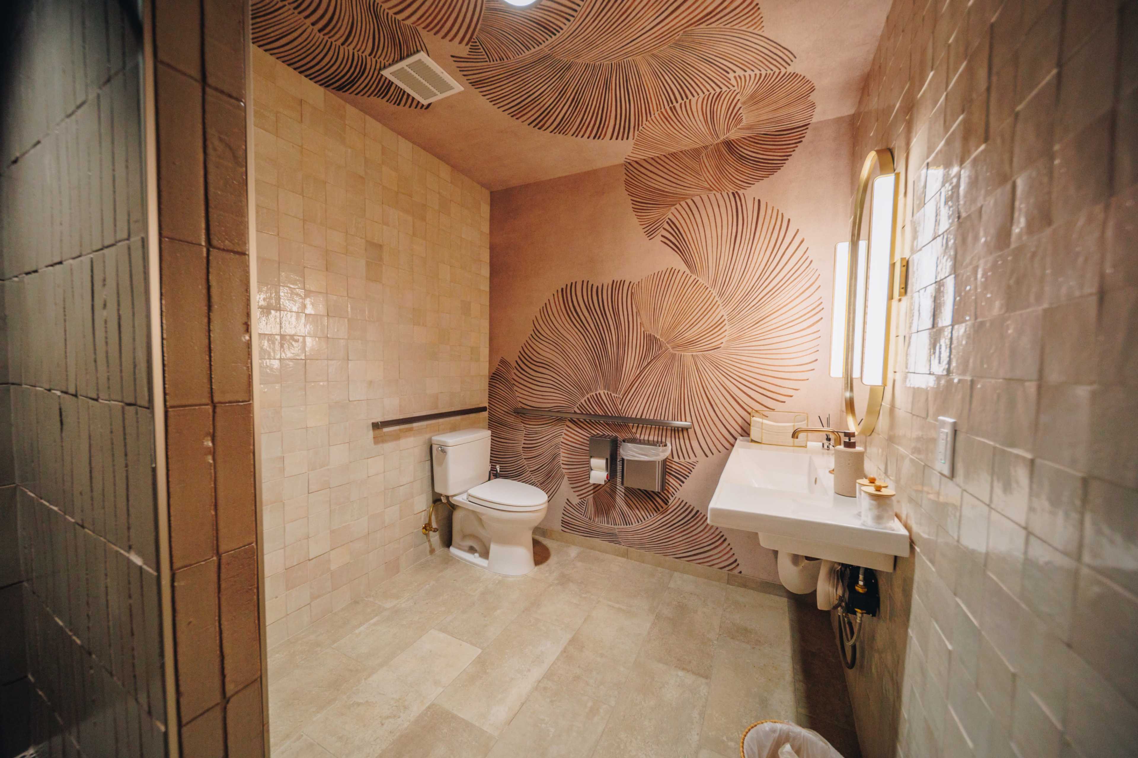 The image shows a spacious bathroom featuring a large decorative wall mural, a toilet, and a sink with a mirror.